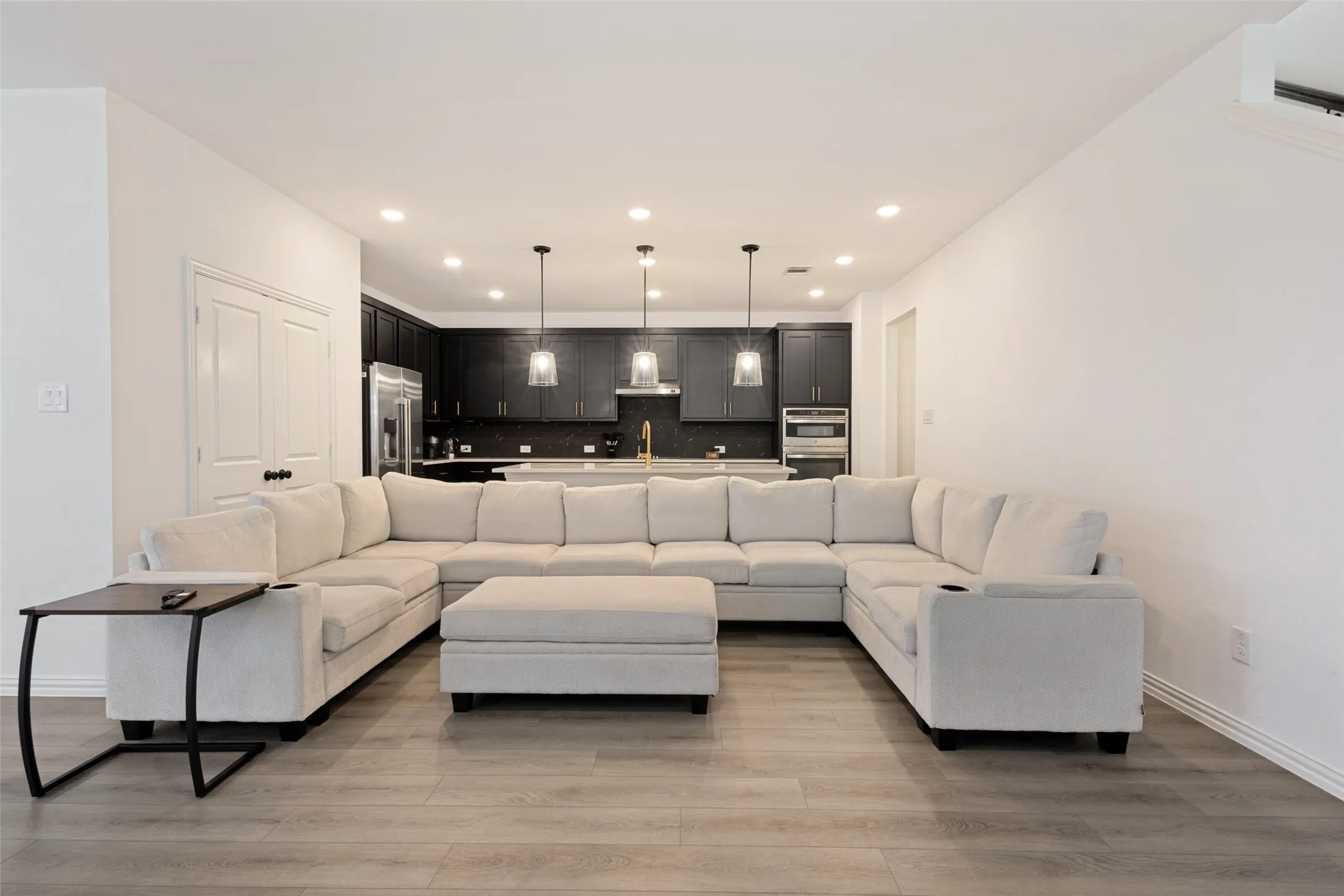 Open-concept living area featuring wood-finish flooring, recessed lighting, and a kitchen with dark cabinetry, stainless steel appliances, and pendant lighting