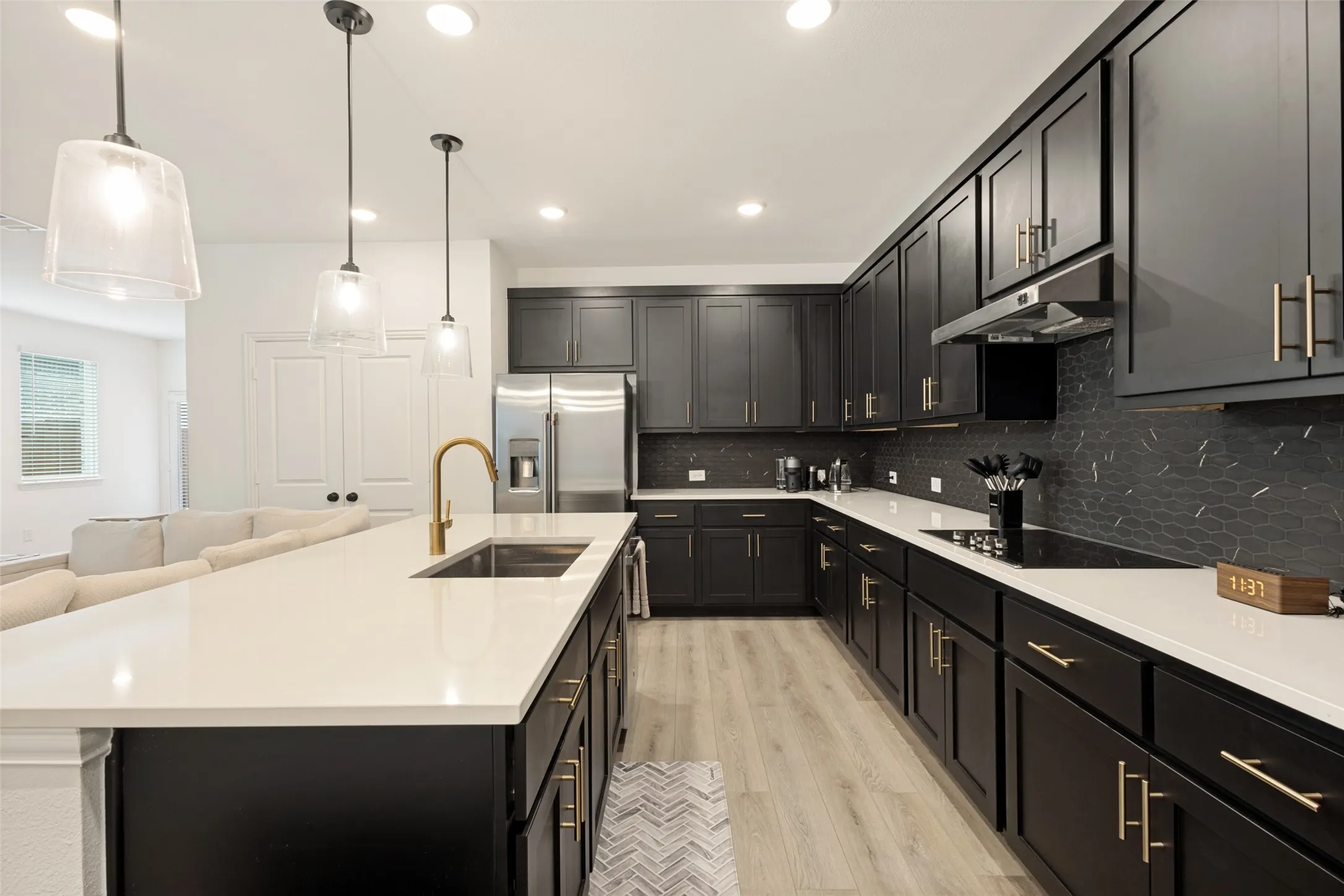 Kitchen featuring dark cabinetry, stainless steel appliances, a large center island with a sink, light-toned countertops, and wood-finish flooring