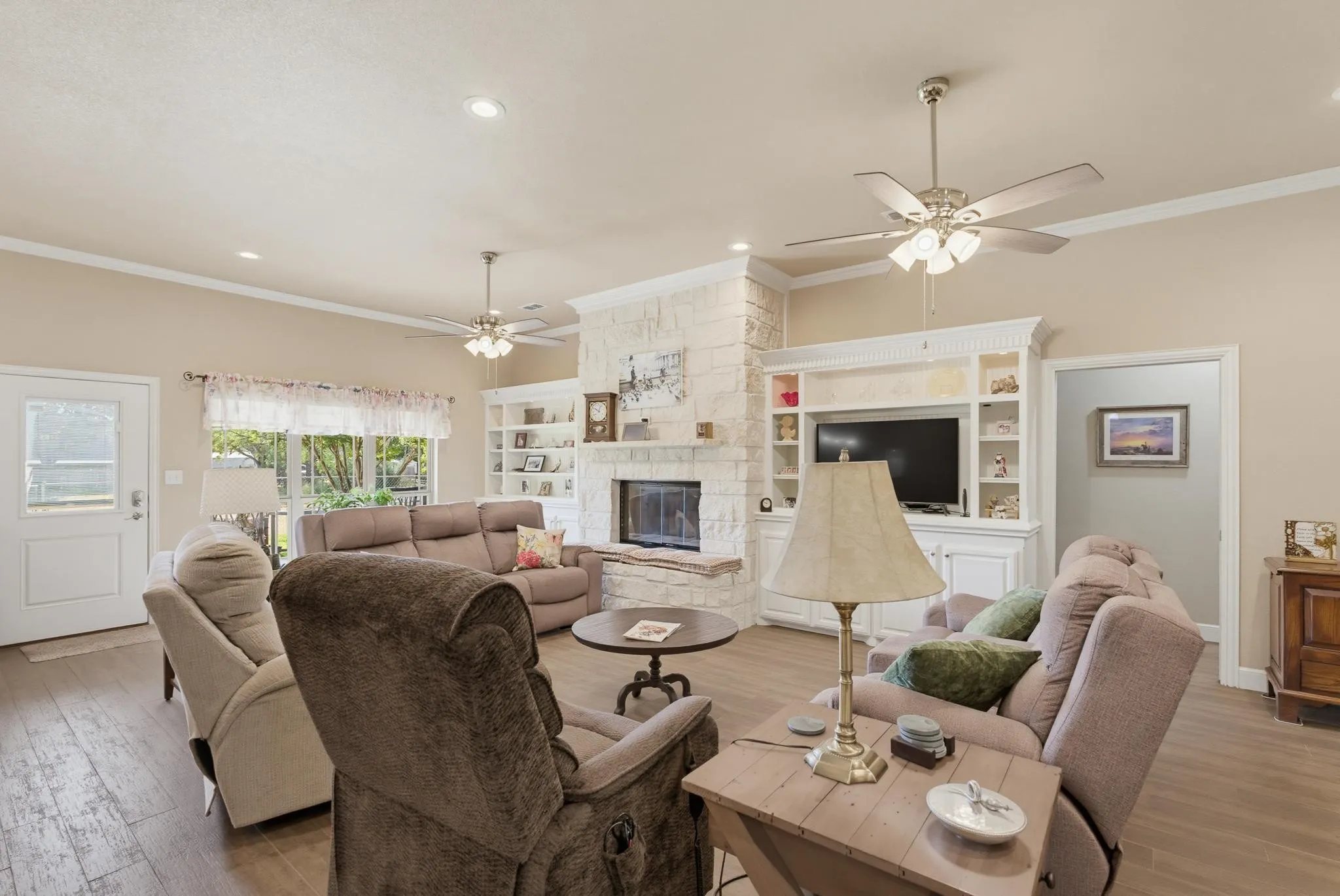 Spacious living area featuring a stone-clad fireplace, integrated shelving, wood-finish flooring, and crown molding
