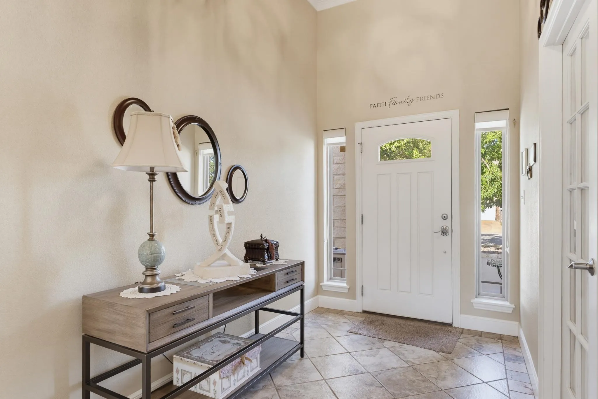 Tiled entry flooring, vaulted ceiling, white paneled door with arched glass insert, and vertical sidelight windows