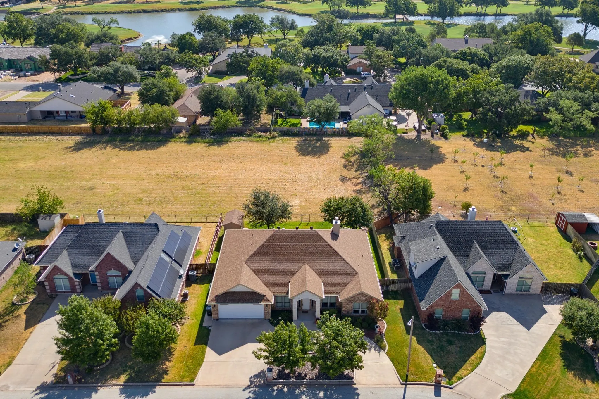 Overhead property view featuring a shingle roof, attached garage, paved driveway, and mature landscaping
