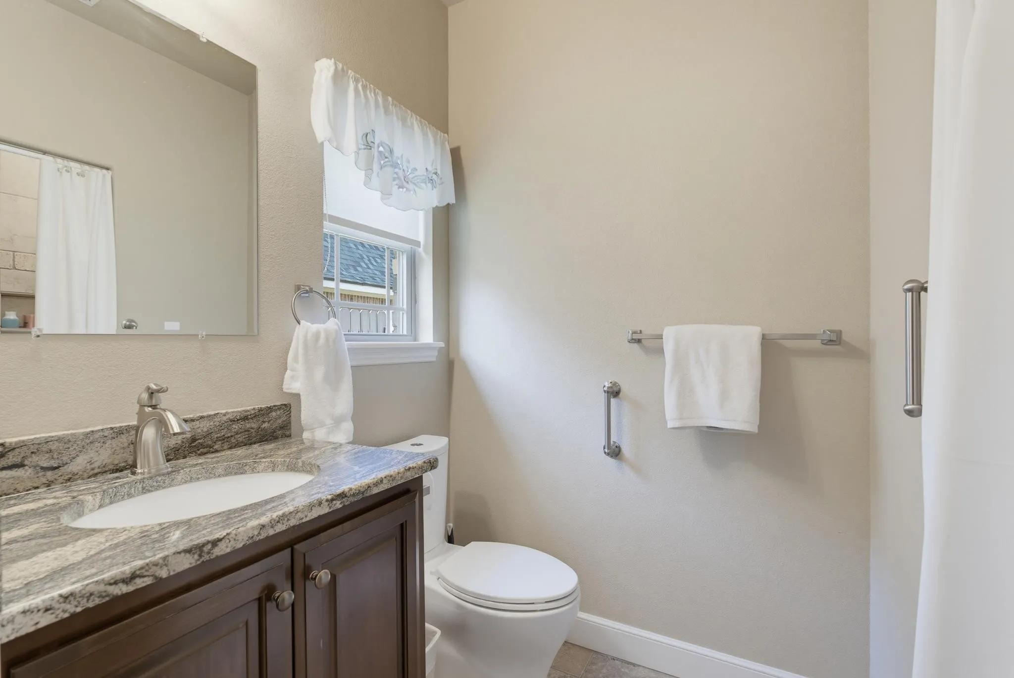 Vanity with an undermount sink and a stone-finish countertop, brushed nickel faucet, and a wall-mounted mirror