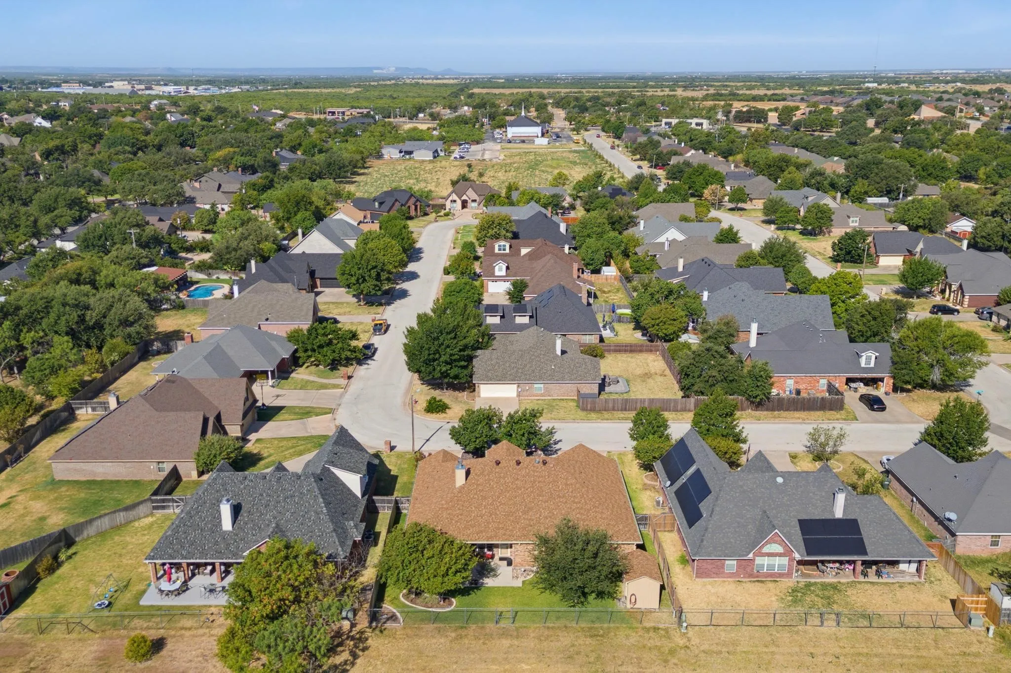 Residential neighborhood with varied rooflines, mature trees, and individual properties featuring fenced yards