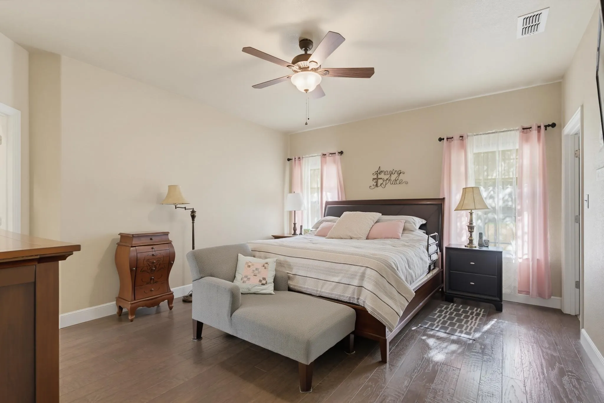 Spacious primary bedroom with wood-finish flooring, ceiling fan with integrated lighting, and glass sliding doors providing natural light