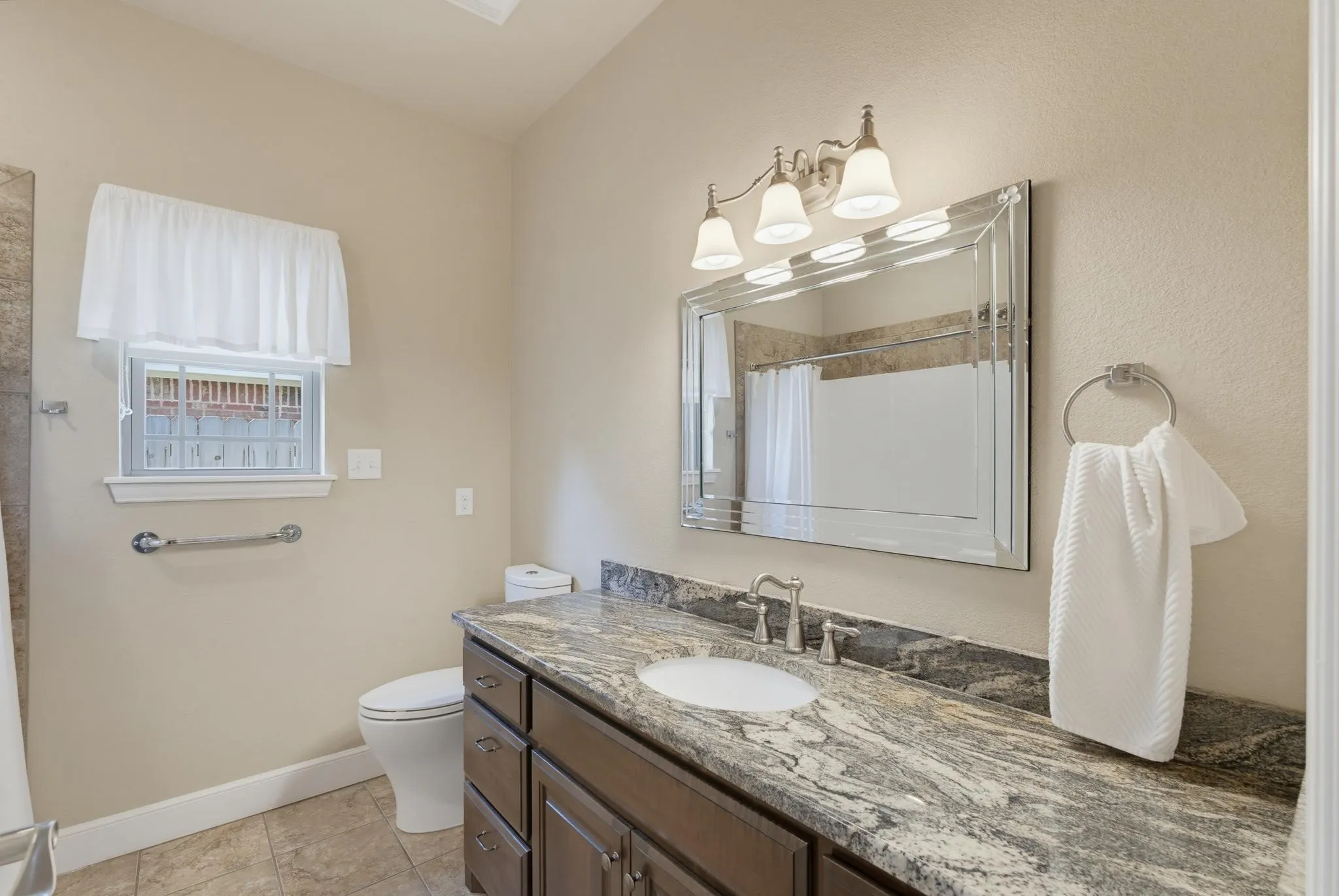 Elegant bathroom featuring a dark wood vanity with dual-sink configuration, granite-finish countertop, and brushed nickel hardware