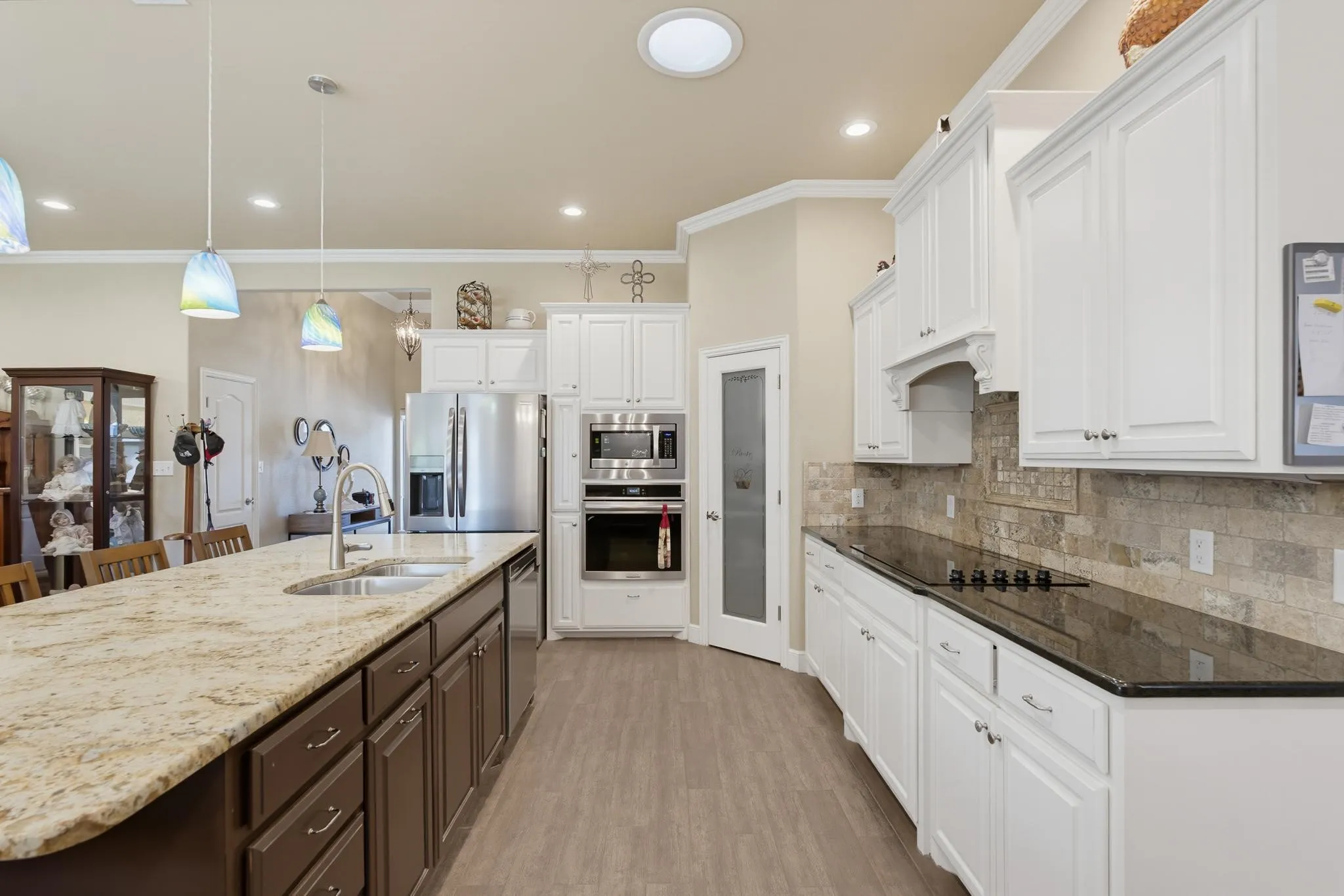Expansive kitchen featuring a large island with dual sinks, white upper and lower cabinetry, black countertops, and wood-finish flooring