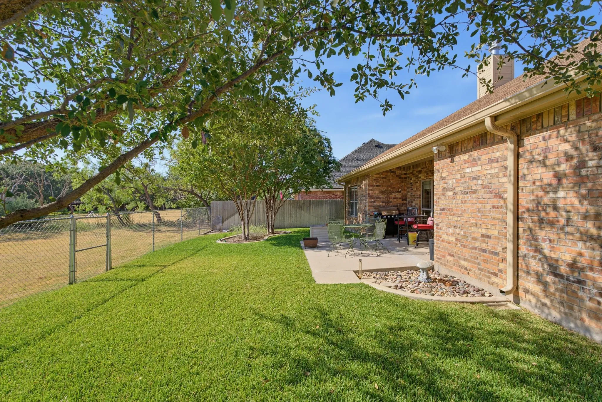Expansive grassy yard with a chain-link fence, mature trees, and a concrete patio