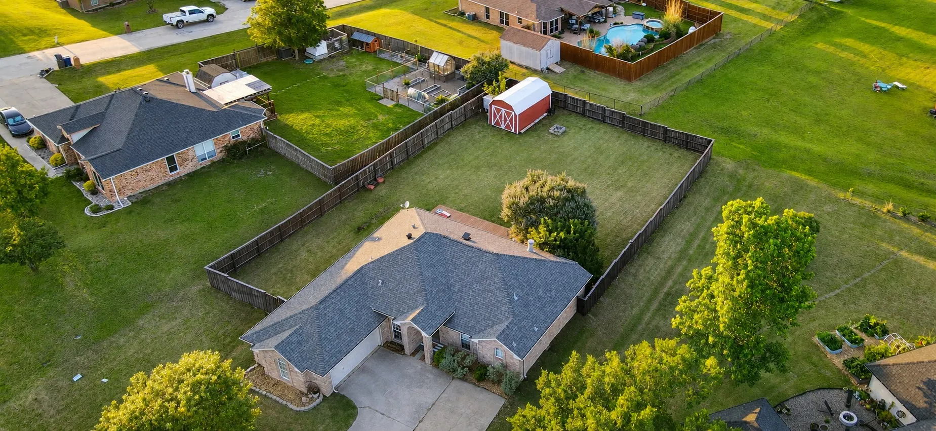 Spacious property featuring a large green lawn, a dark shingle roof, a red barn-style shed, and a privacy fence enclosing the backyard