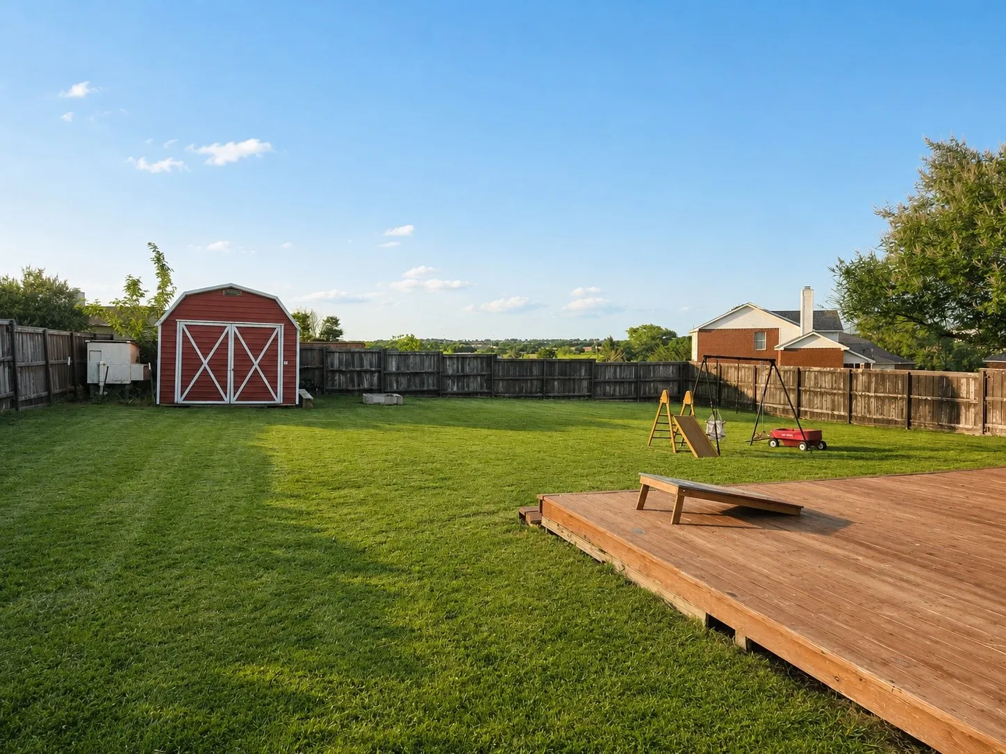 Expansive backyard featuring a wood deck, red storage shed, and perimeter wood fencing