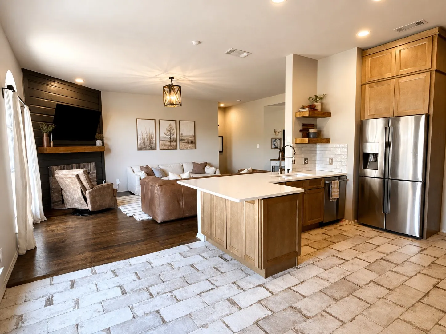 Open-concept living space featuring a kitchen island with light-toned countertop, a stainless steel refrigerator, and wood-finish cabinetry