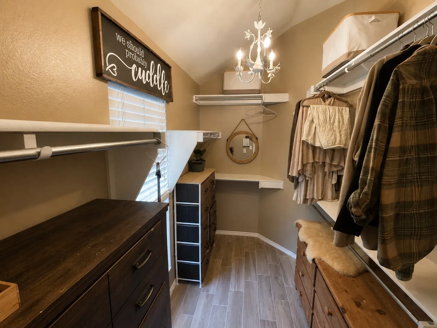 Custom closet organization system featuring light wood-finish flooring, a decorative chandelier, multiple hanging rods, and integrated shelving