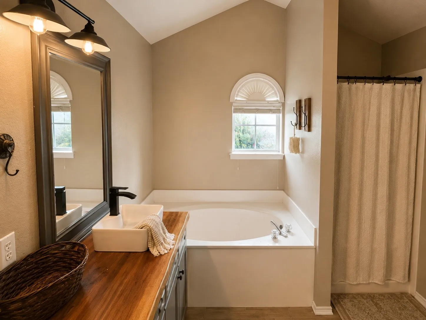 Spacious bathroom featuring a built-in soaking tub, a vaulted ceiling, and a vanity with a wood-finish countertop
