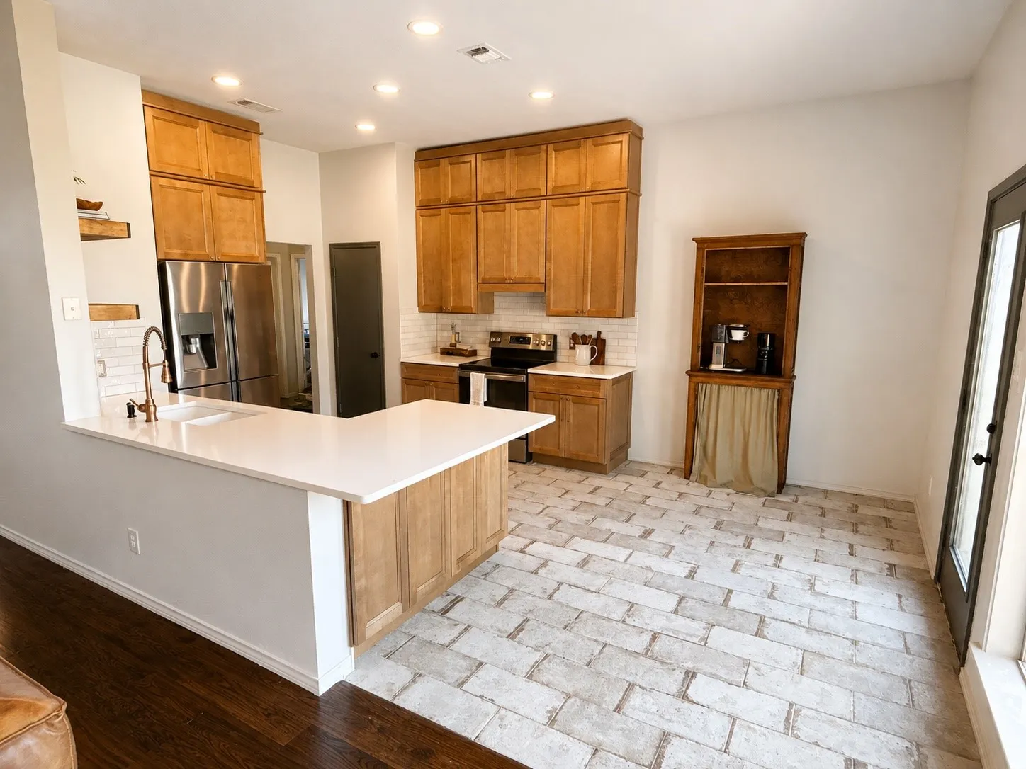 Kitchen featuring light wood cabinetry, a white subway tile backsplash, and a large L-shaped island with a white countertop