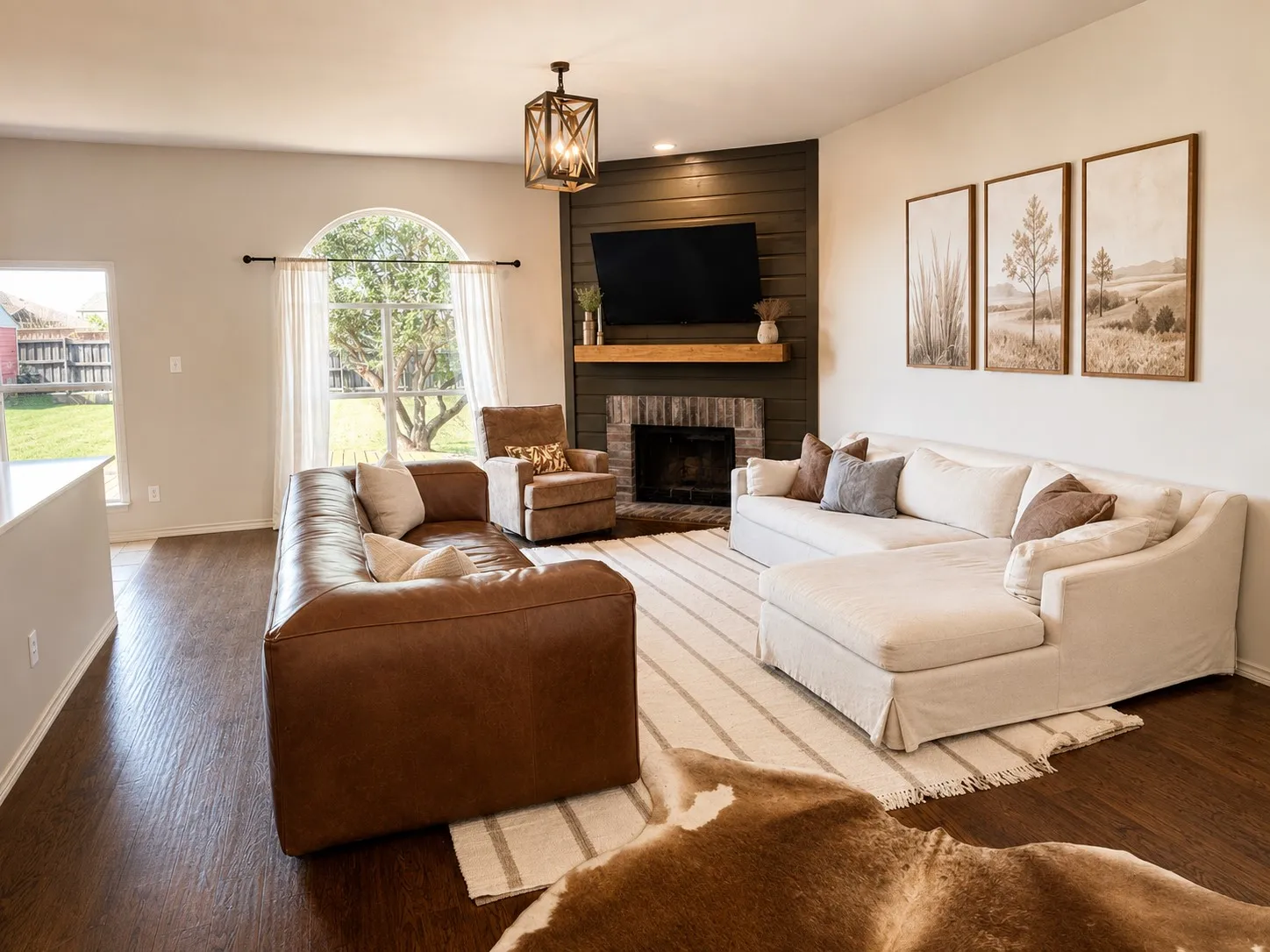 Spacious living area featuring rich wood-finish flooring, a prominent fireplace with a brick surround and wood mantle, and a dark accent wall