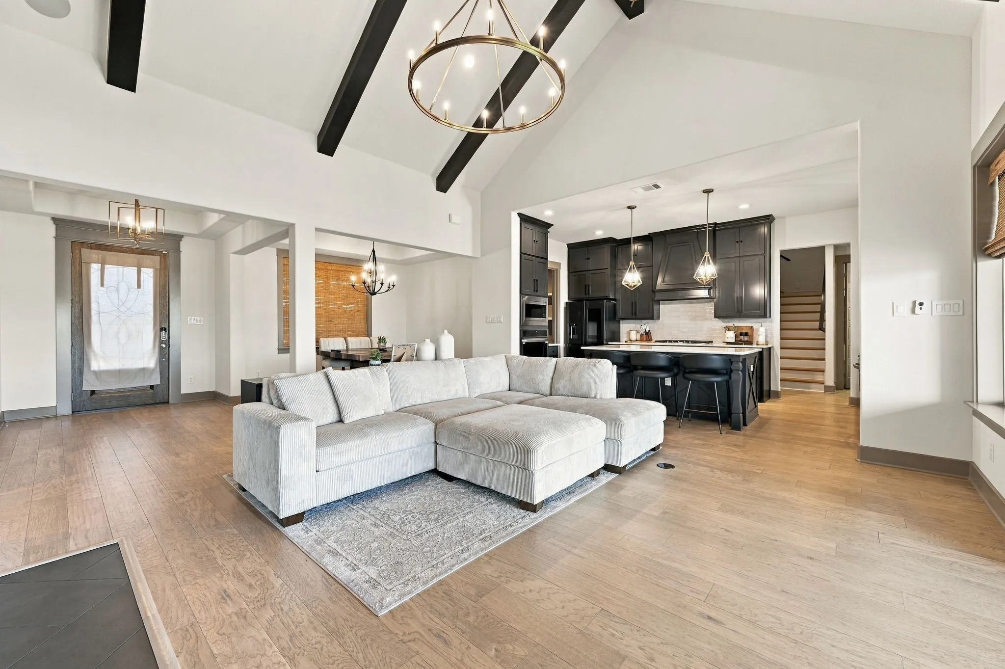Vaulted ceilings with exposed beams, wood-finish flooring, recessed lighting, kitchen with dark cabinetry, and an island with pendant lighting