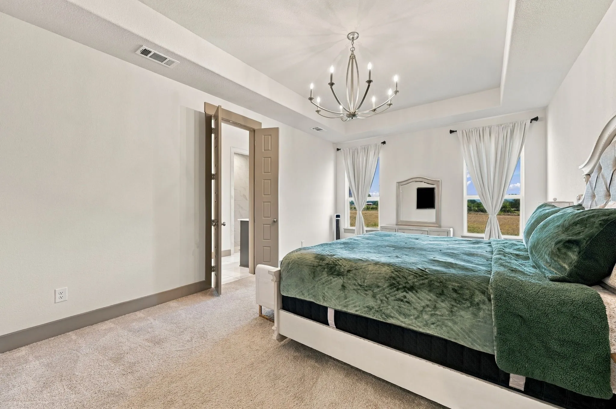 Tray ceiling with a decorative chandelier, carpeted flooring, and two windows