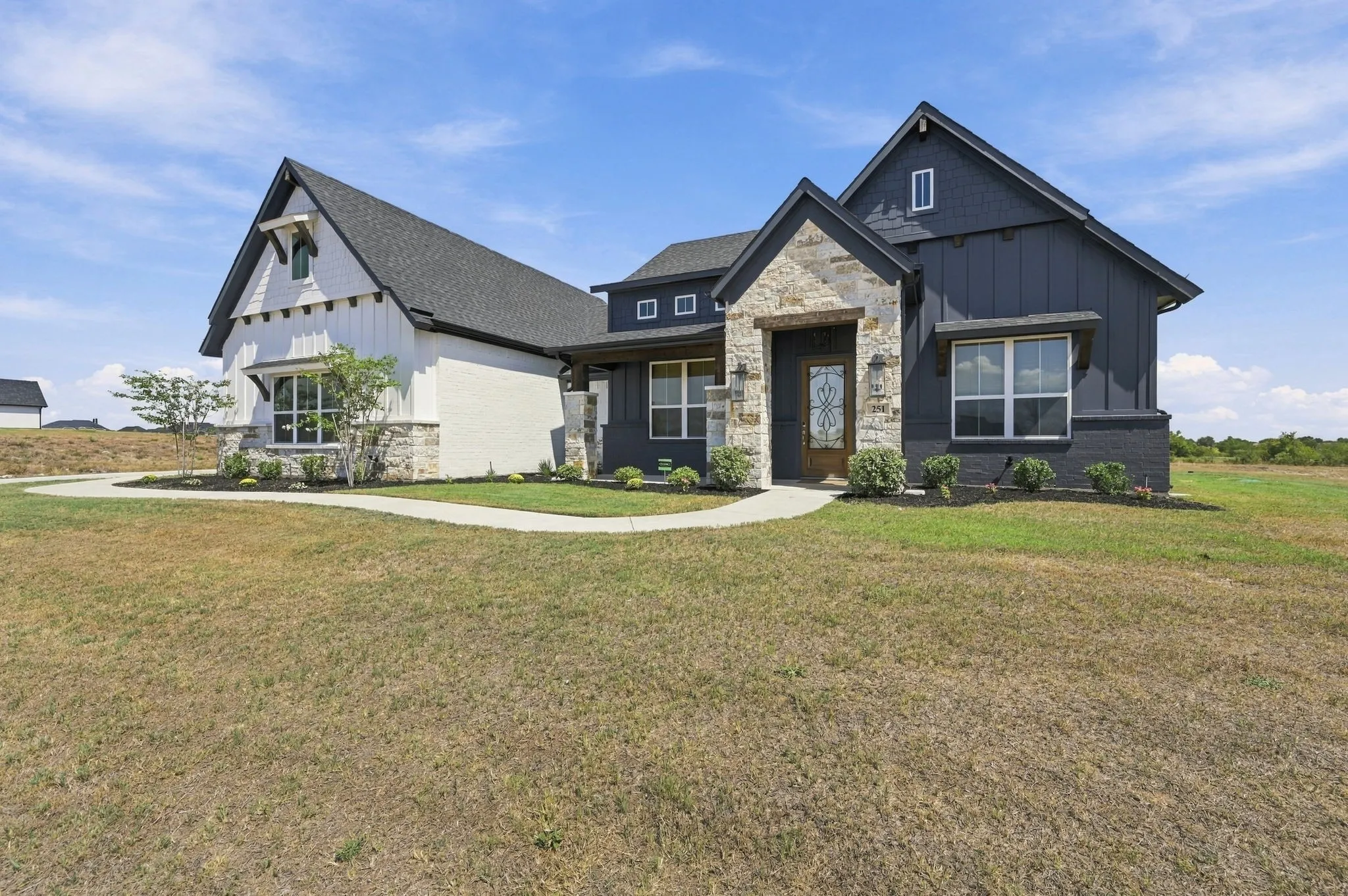 Exterior featuring stone accents, dark board and batten siding, white vertical siding, and an ornate glass panel entry door