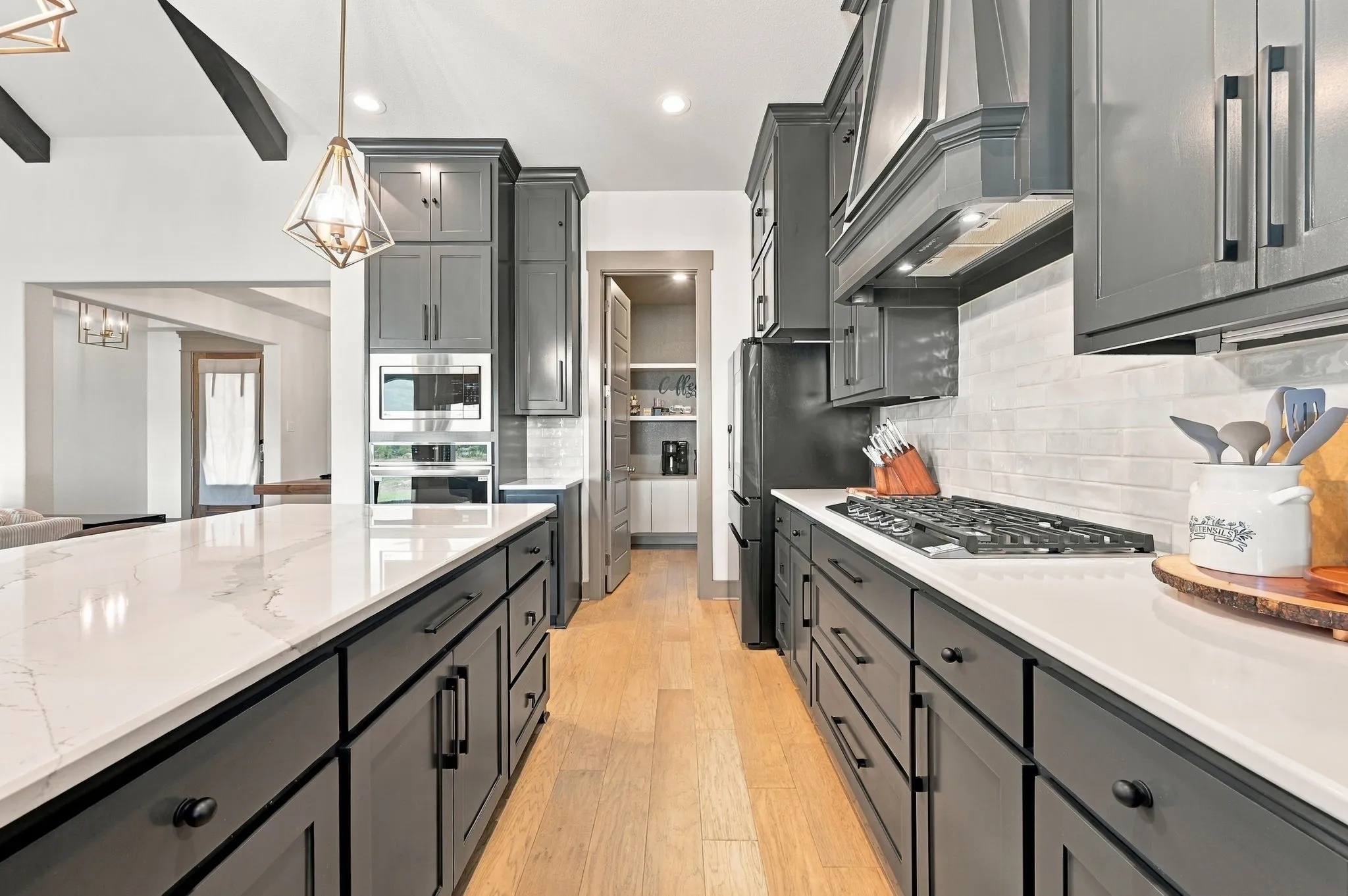 Spacious kitchen featuring an expansive island with a white countertop, dark shaker-style cabinetry, stainless steel appliances, and wood-finish flooring