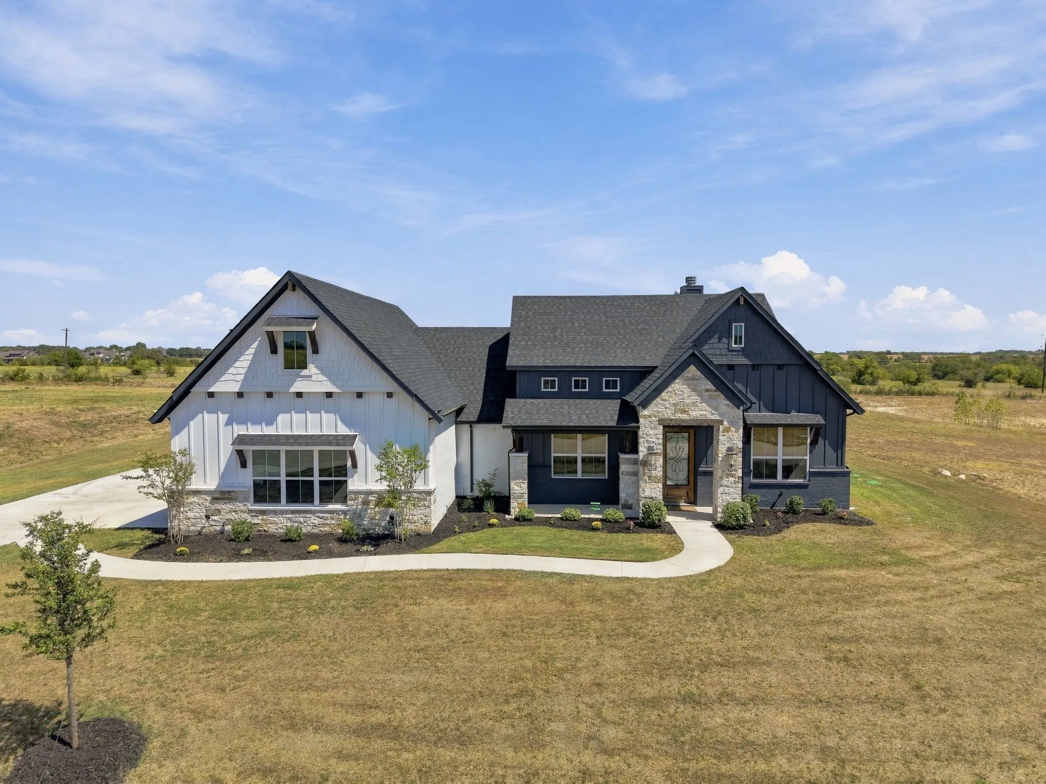 Modern farmhouse exterior featuring dark gray siding, white board-and-batten siding, stone accents, black-trimmed windows, and a dark asphalt shingle roof