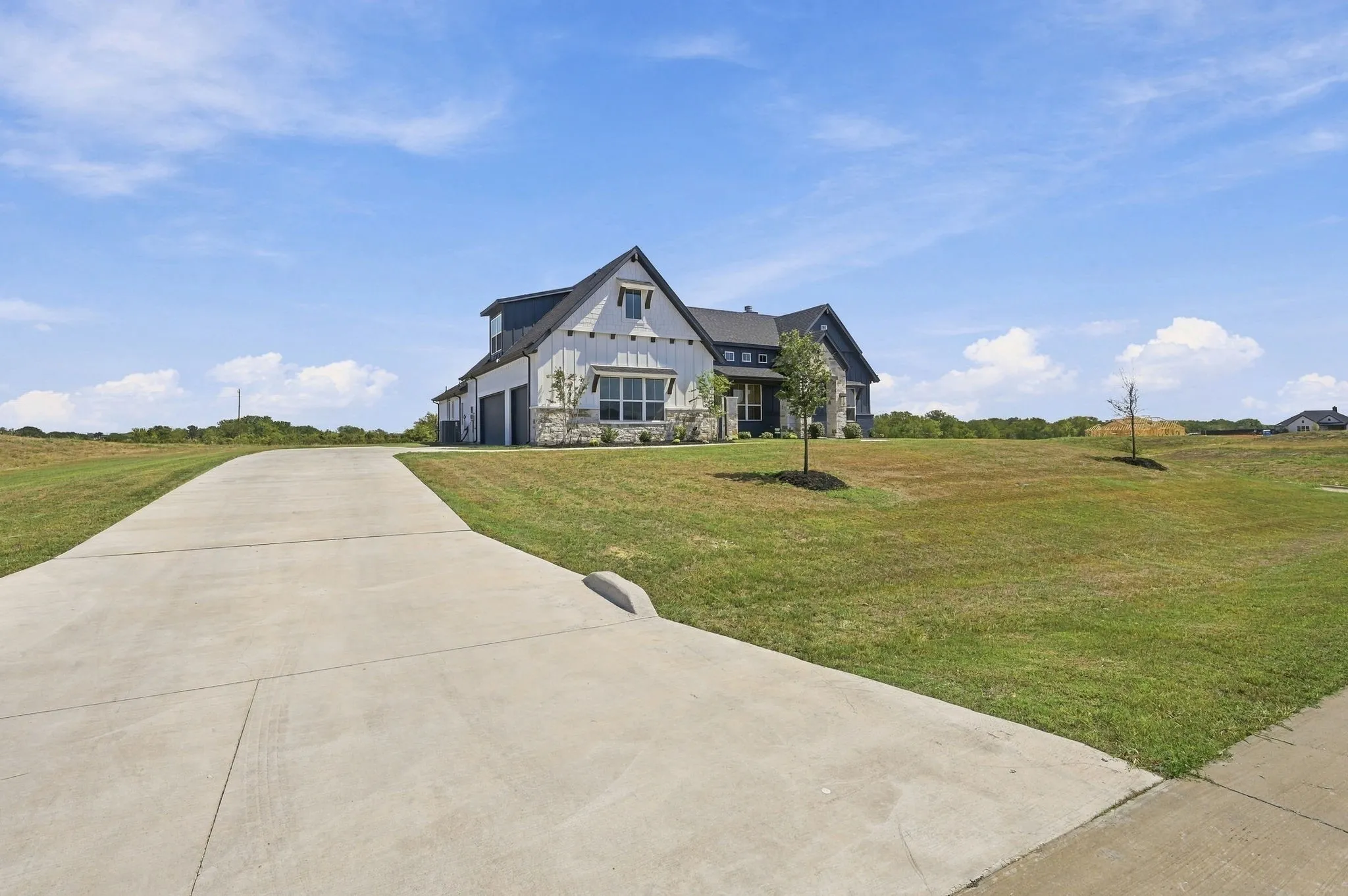 Modern farmhouse style residence with a concrete driveway, stone facade accents, dark framed windows, and a multi-car garage