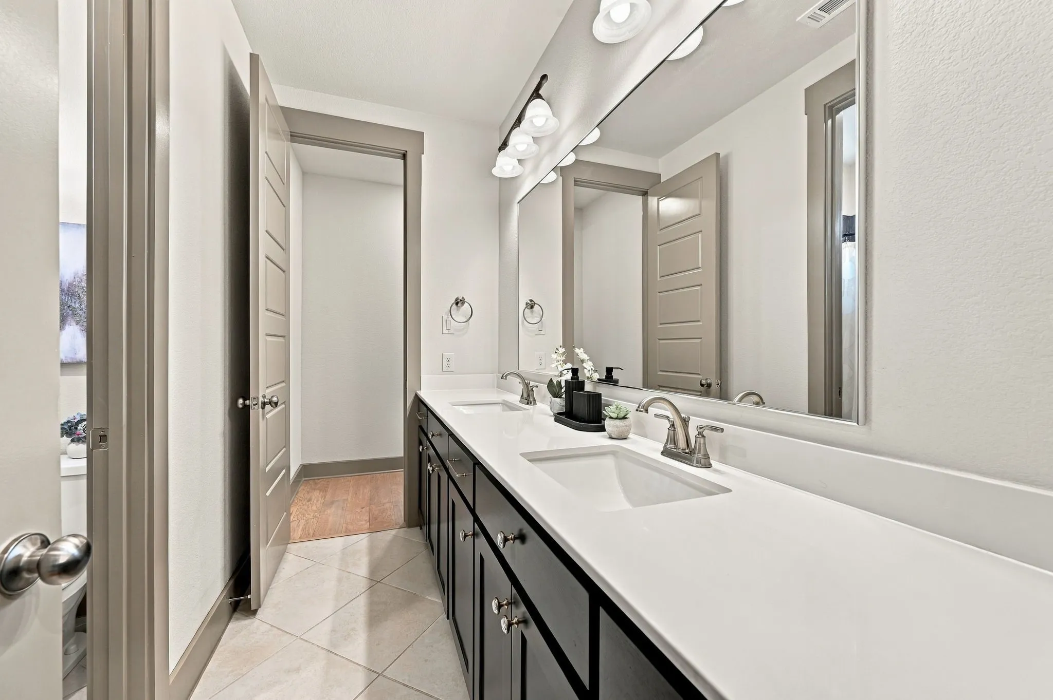 Dual vanity with integrated sinks, expansive counter space, dark wood-finish cabinetry, brushed nickel fixtures, and decorative tile flooring
