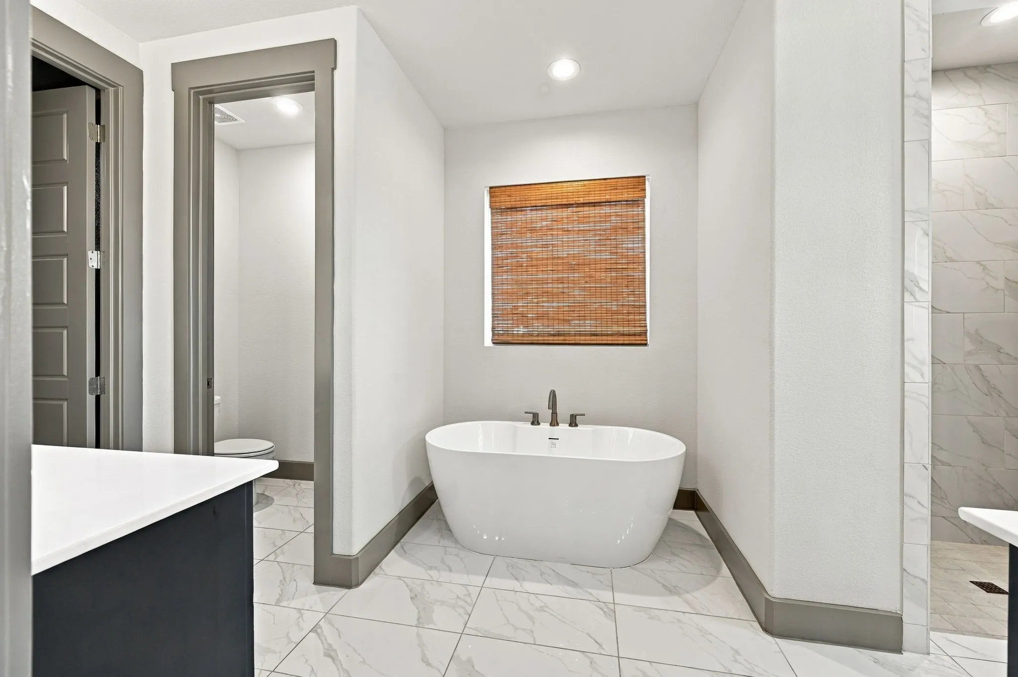 Freestanding soaking tub with floor-mounted faucet, marble-look tile flooring, and a walk-in shower with matching tile