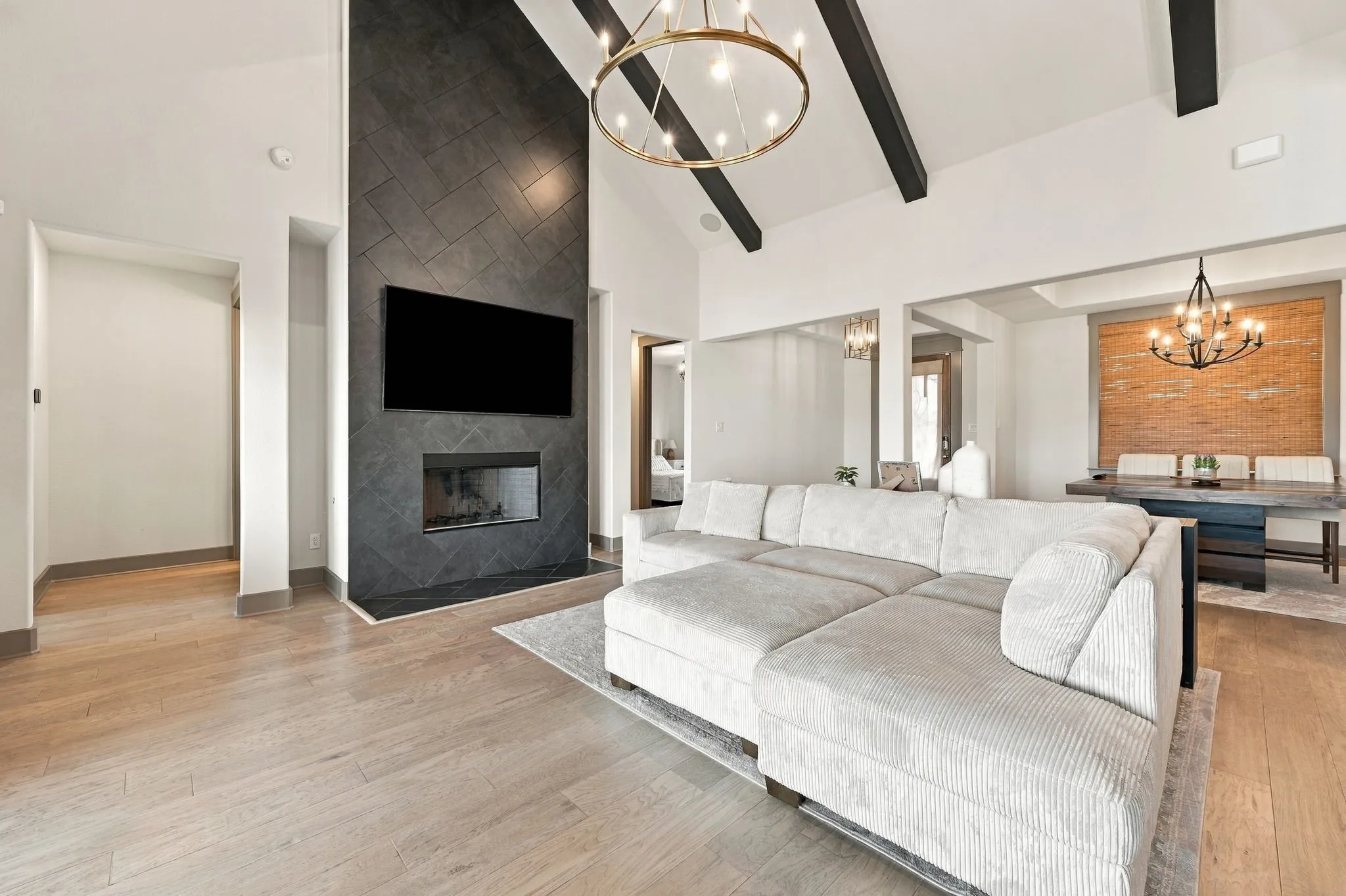 Vaulted ceilings with exposed beams, wood-finish flooring, and a modern fireplace with herringbone tile surround