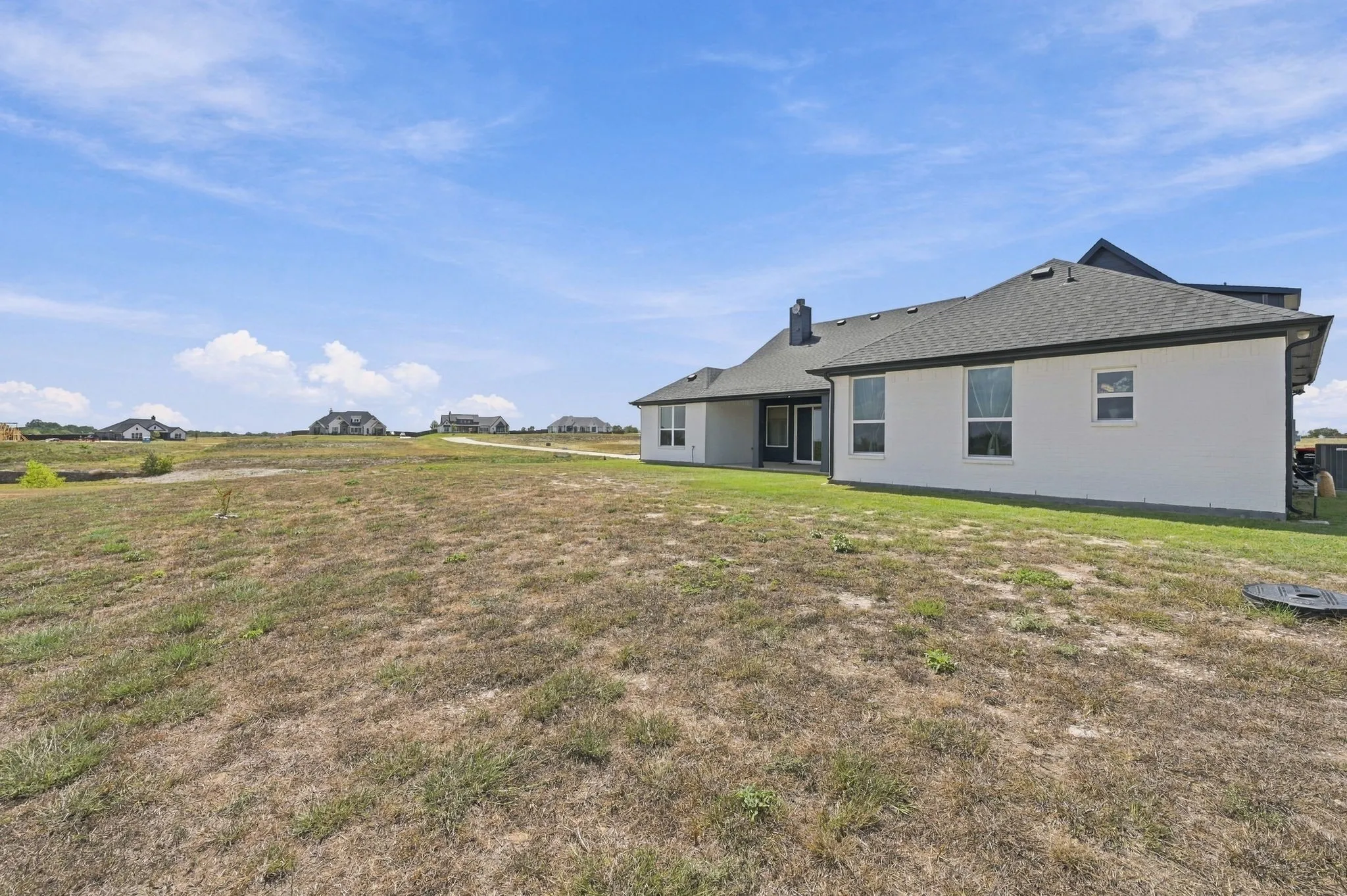 Expansive rear exterior featuring a white stucco finish, multiple large windows, and a dark shingle roof