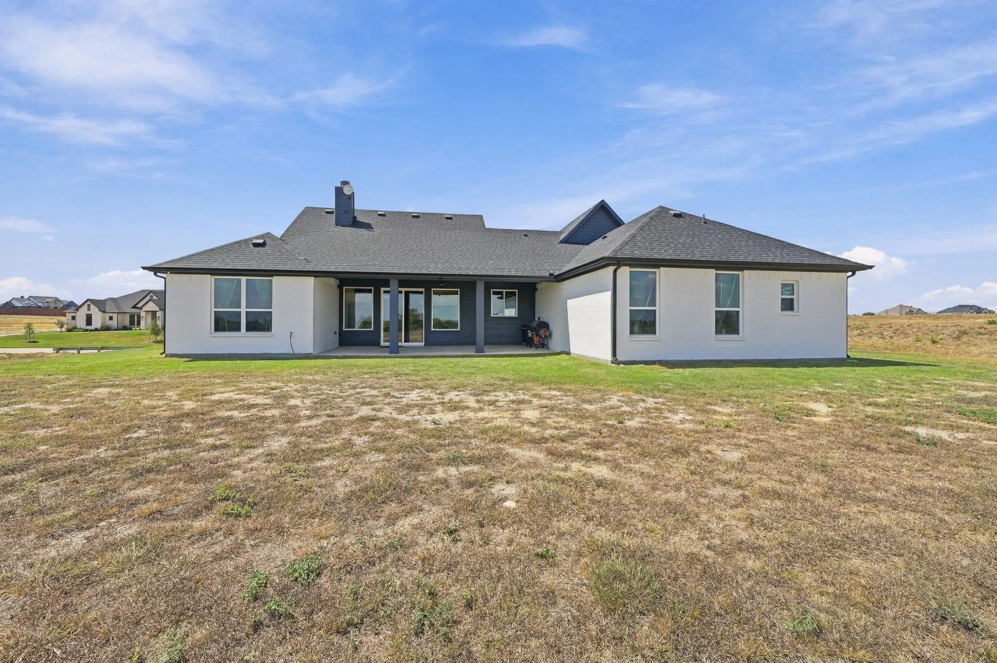 Contemporary exterior with a covered patio, multiple large windows, and a dark shingled roof