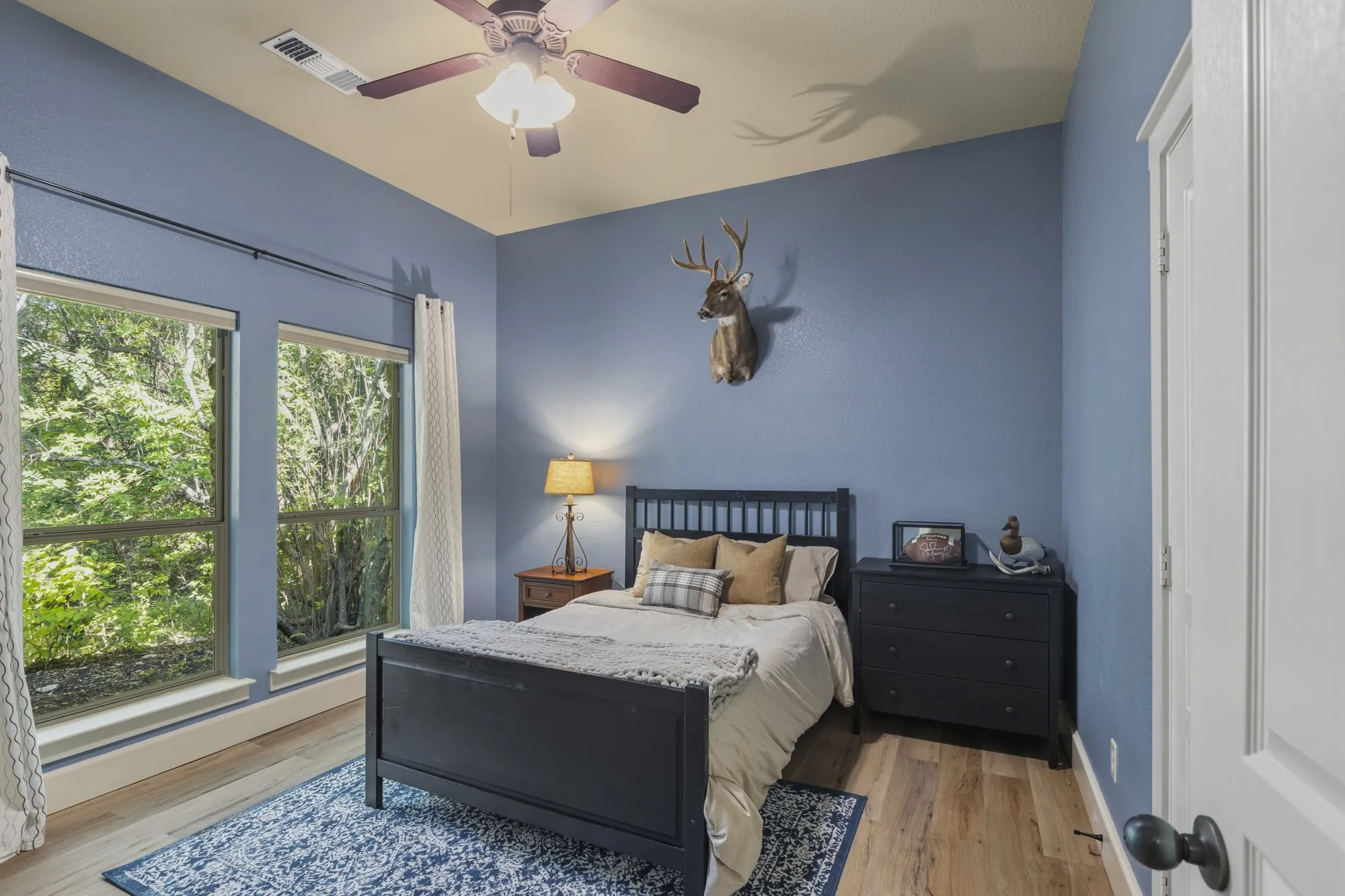 Expansive windows, wood-finish flooring, ceiling fan with integrated lighting, and a white paneled door