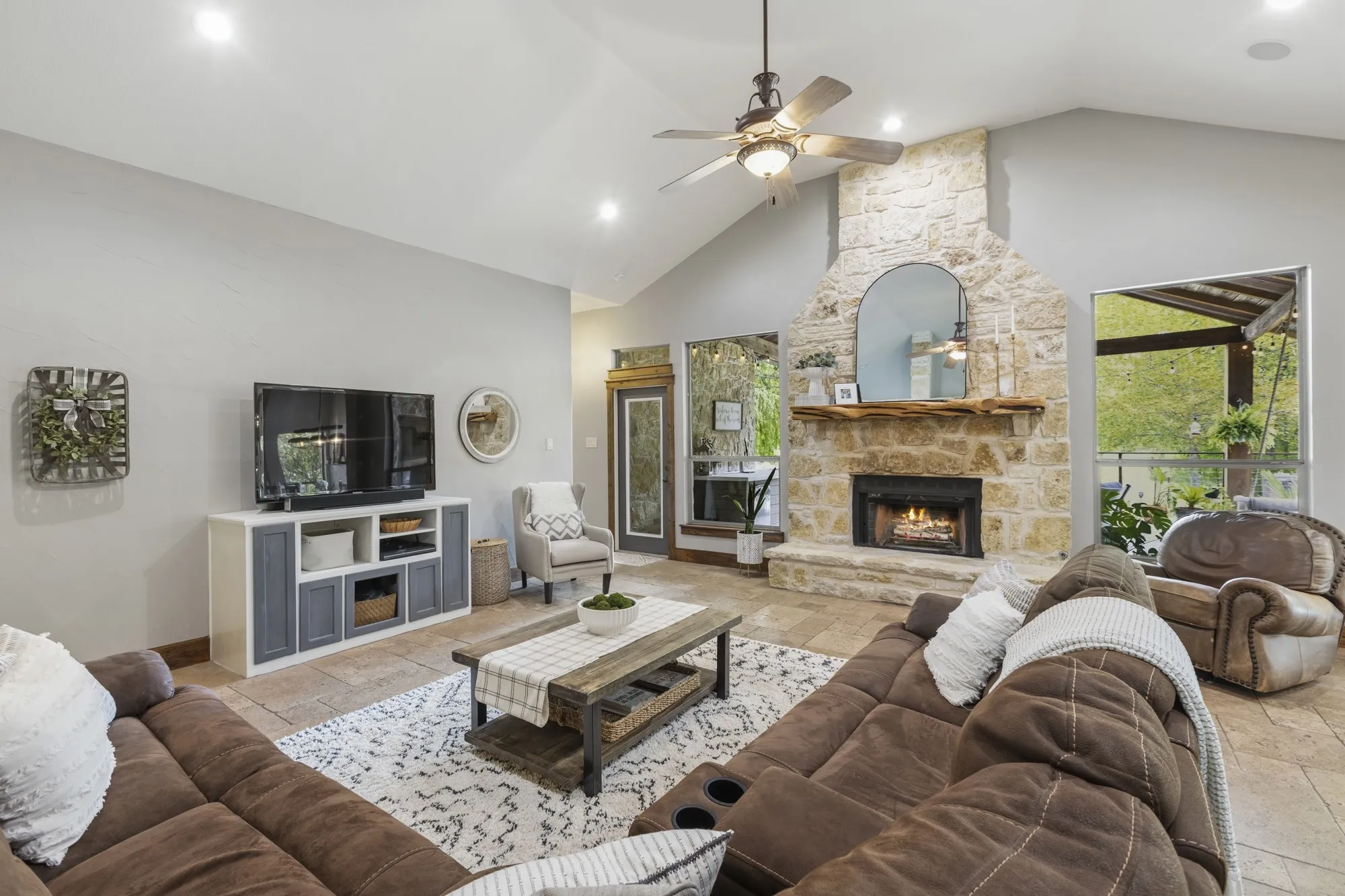 Vaulted ceiling with a ceiling fan, stone fireplace with a wood mantel, recessed lighting, tile flooring, and large windows