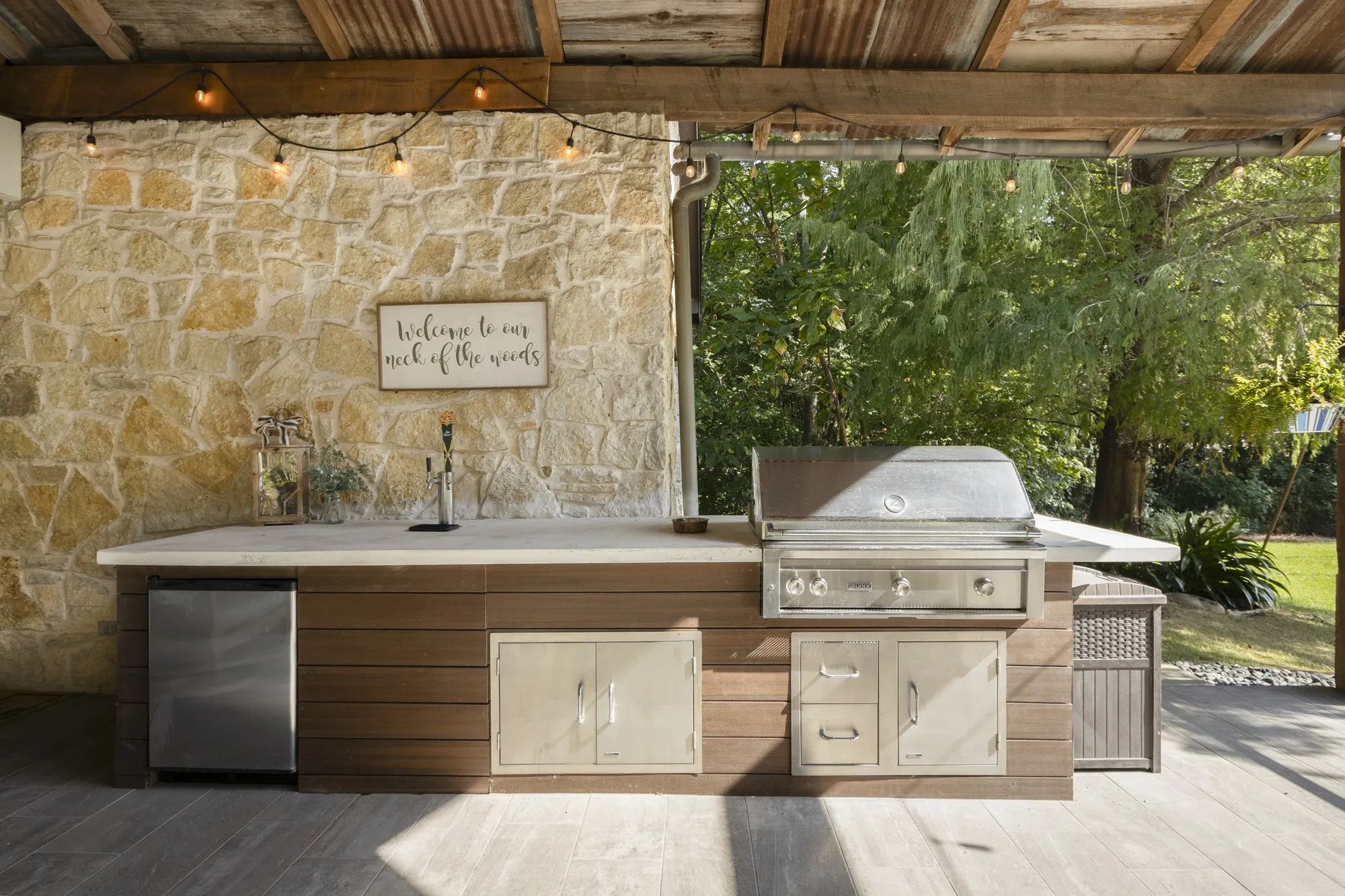 Outdoor kitchen featuring a stone accent wall, built-in stainless steel grill, integrated mini-refrigerator, and ample countertop space