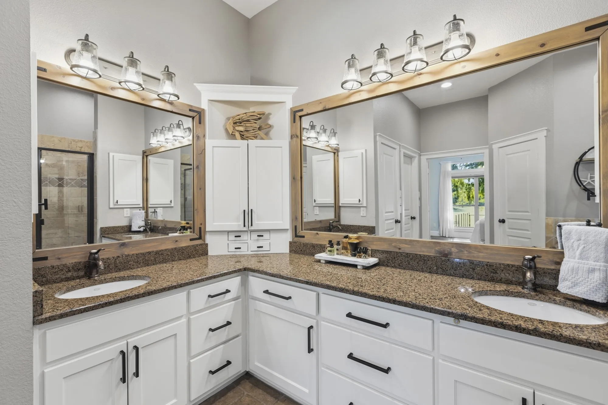 Dual vanity with stone countertops, white cabinetry, dark hardware, and large wood-framed mirrors