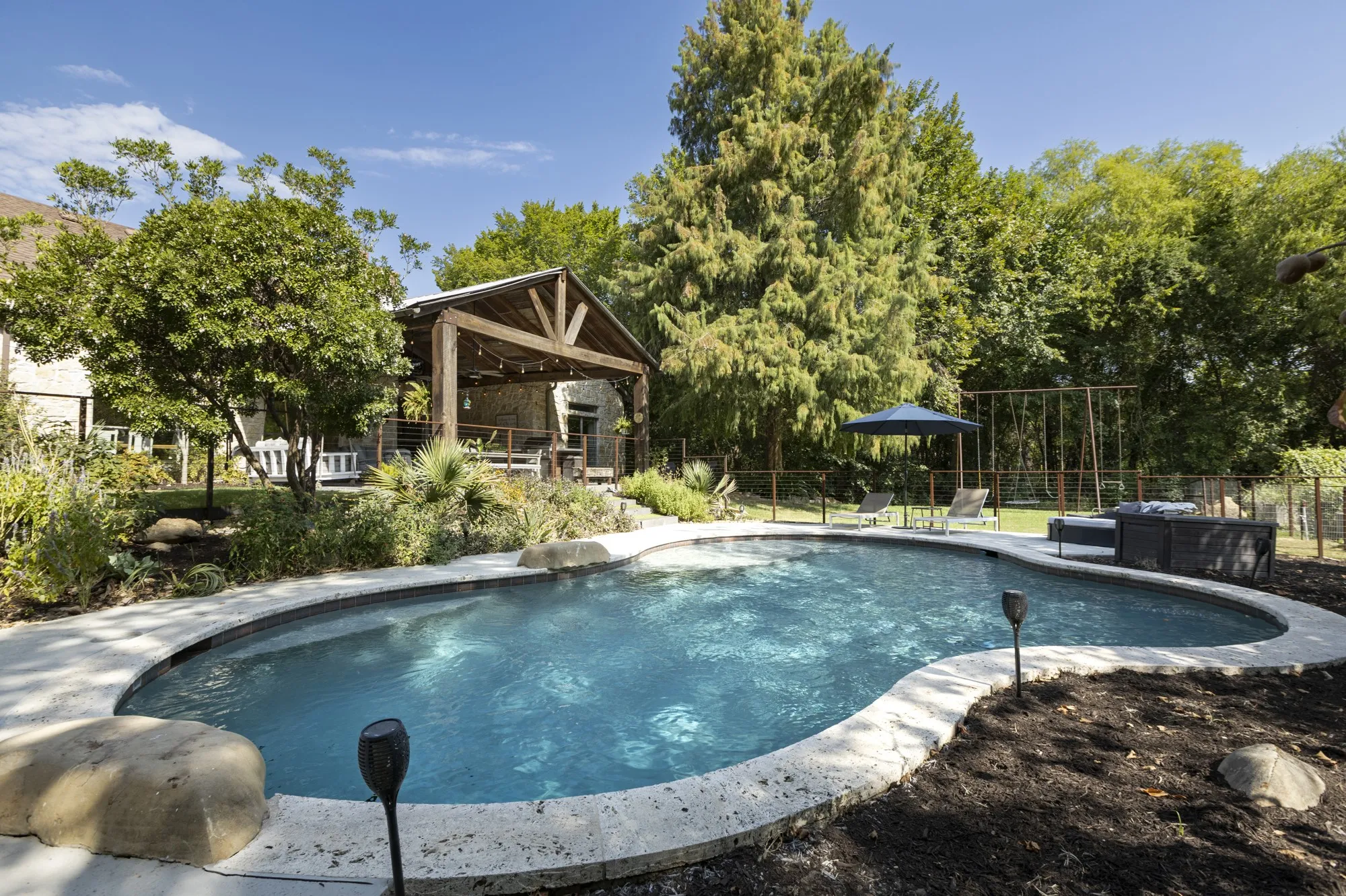 Freeform swimming pool with a stone coping and surrounding landscaping