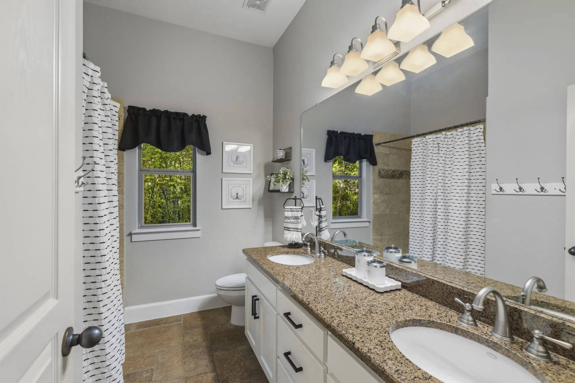 Double vanity with stone countertop, tile flooring, and a tiled shower with a window