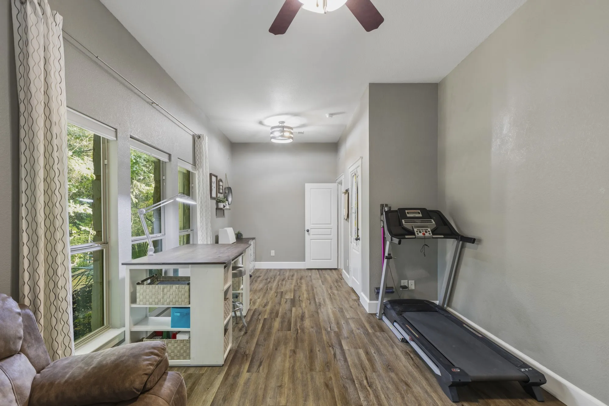 Spacious room featuring wood-finish flooring, multiple windows, and a ceiling fan