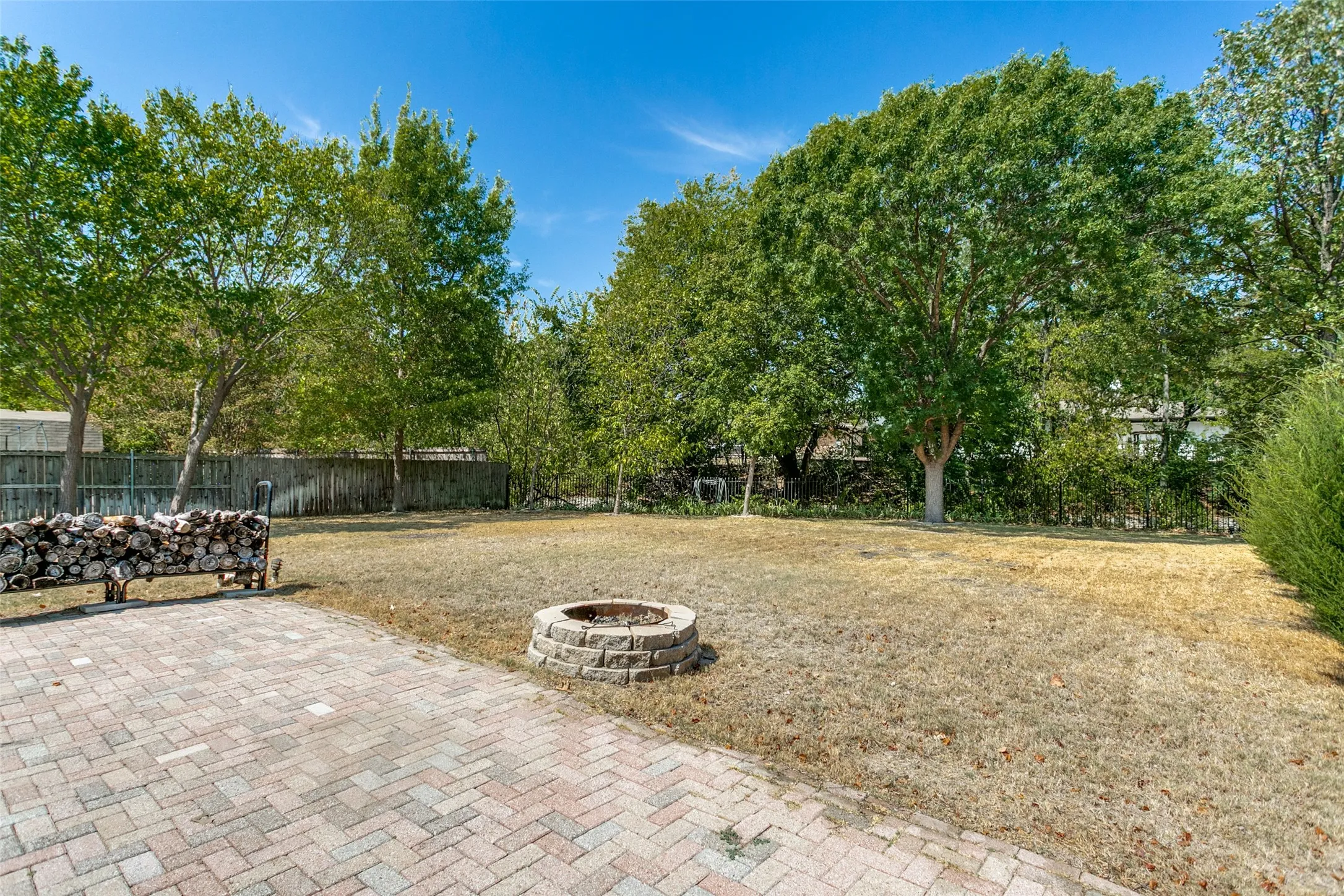 Expansive backyard featuring a paver patio, stone fire pit, and mature trees