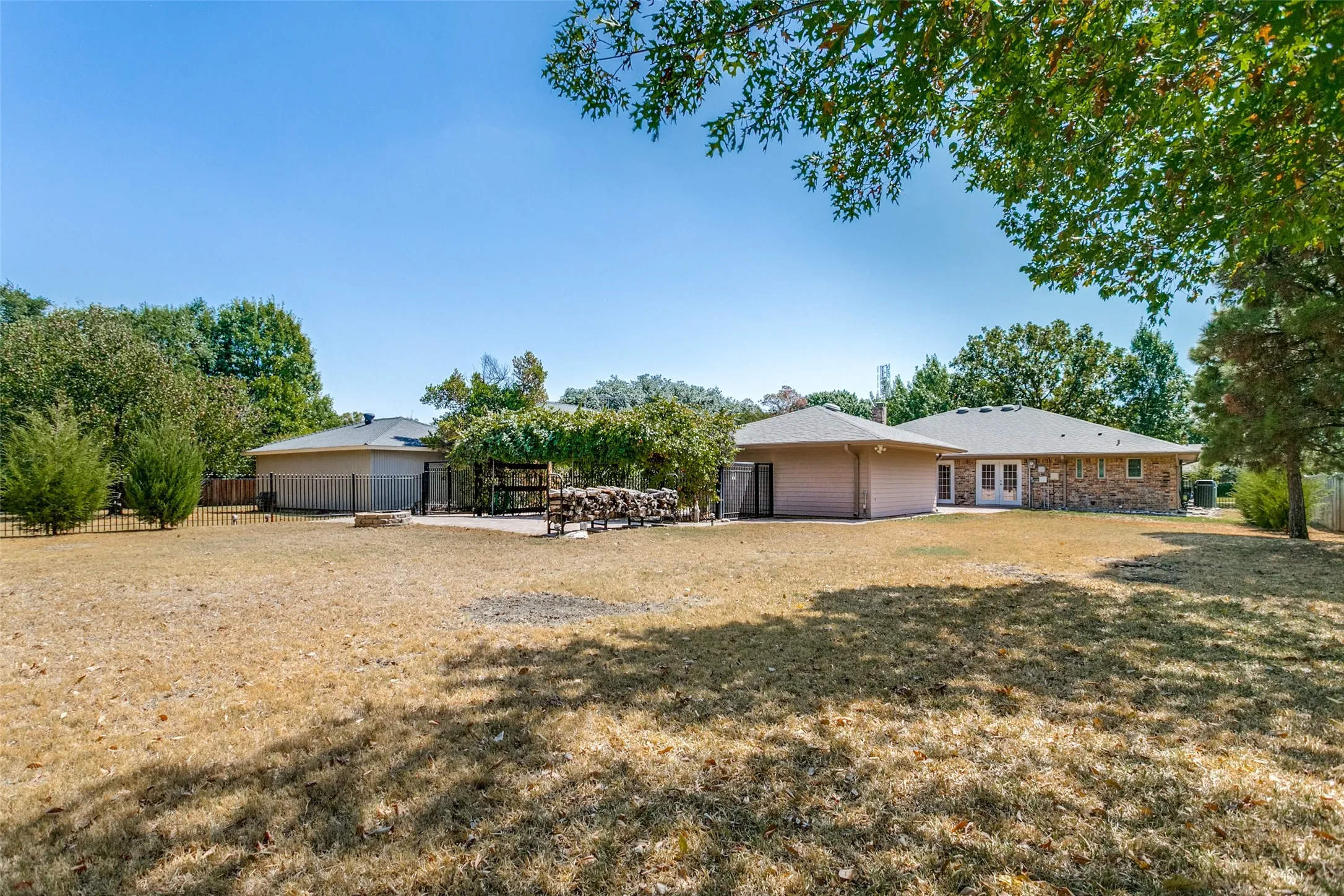 Expansive backyard with a large patio area, two sets of French doors, and mature perimeter trees
