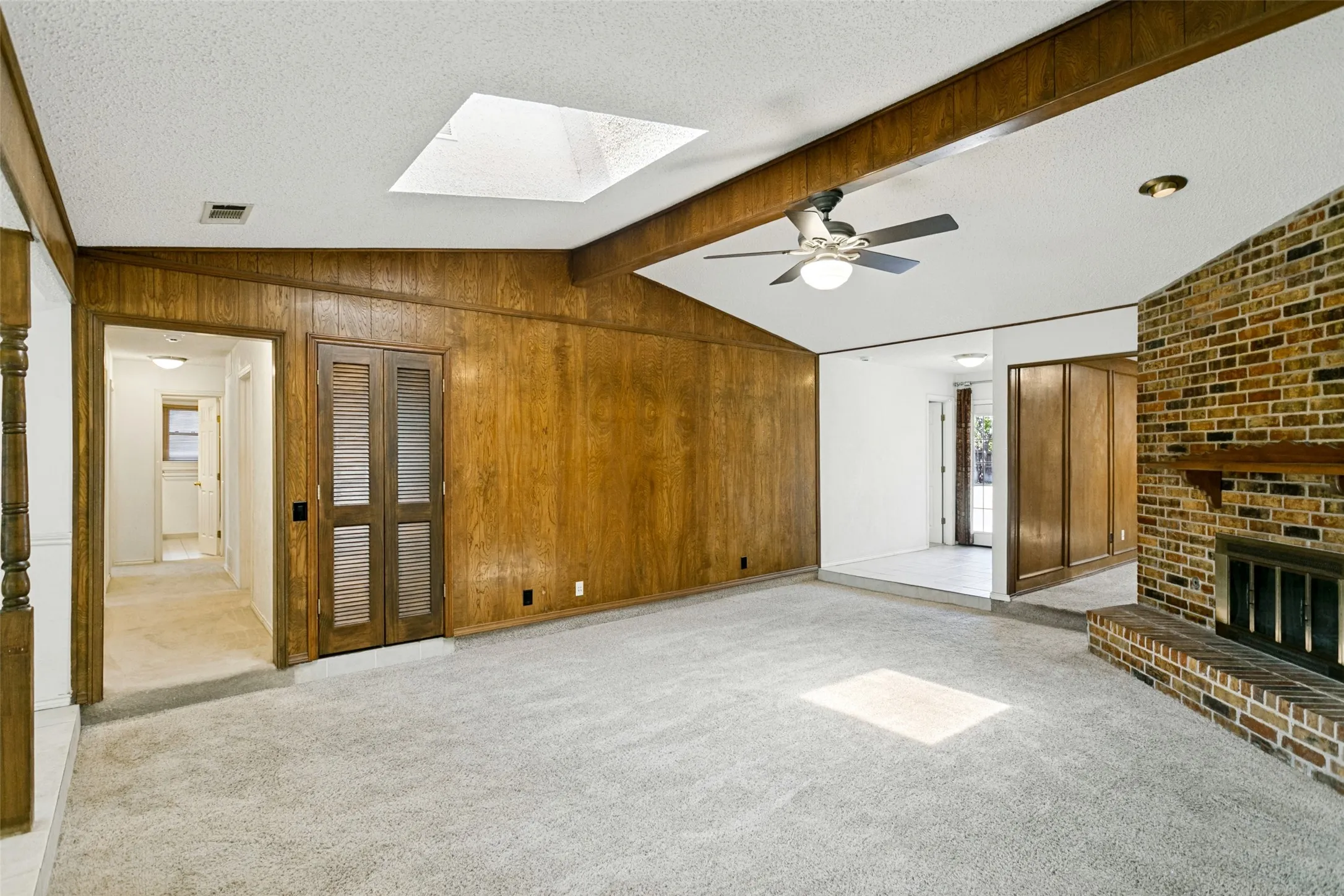 Vaulted ceiling with exposed wood beams, skylight, and ceiling fan