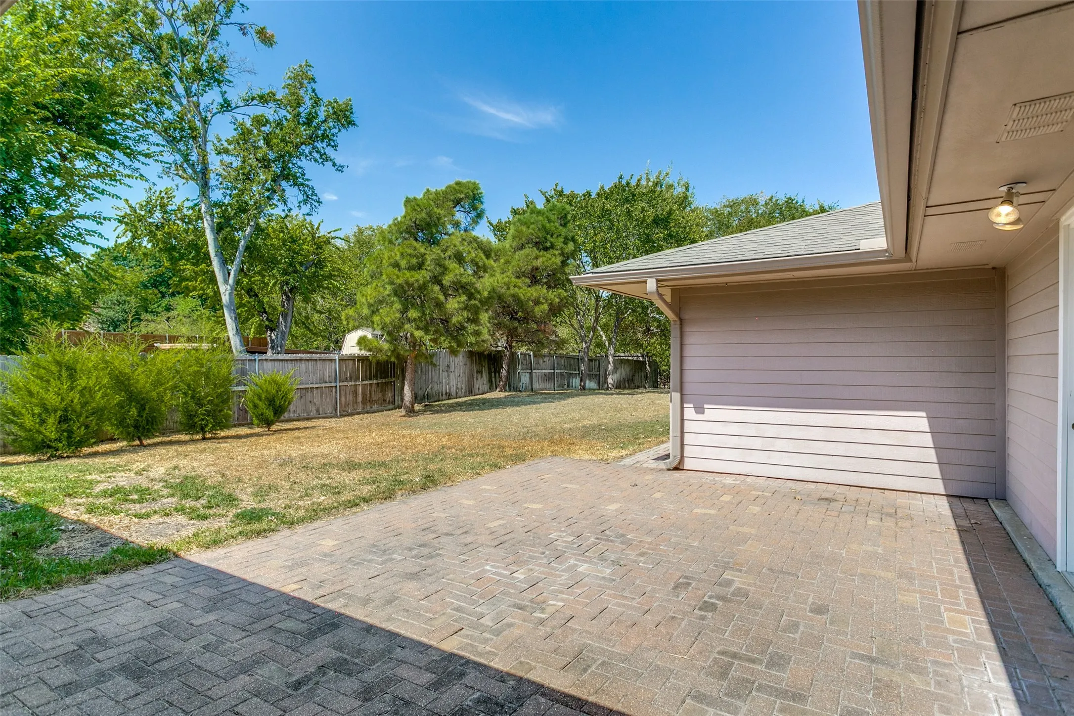 Spacious paver patio with a wood privacy fence and mature landscaping