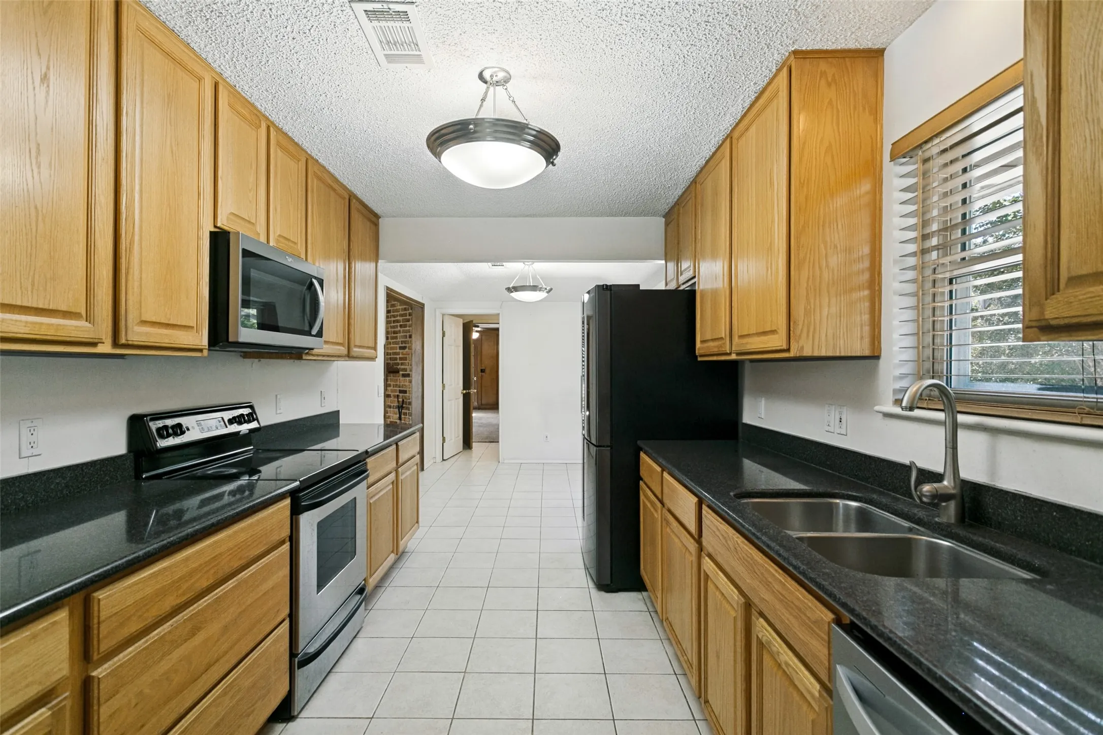 Galley kitchen with light wood cabinetry, dark countertops, and tile flooring