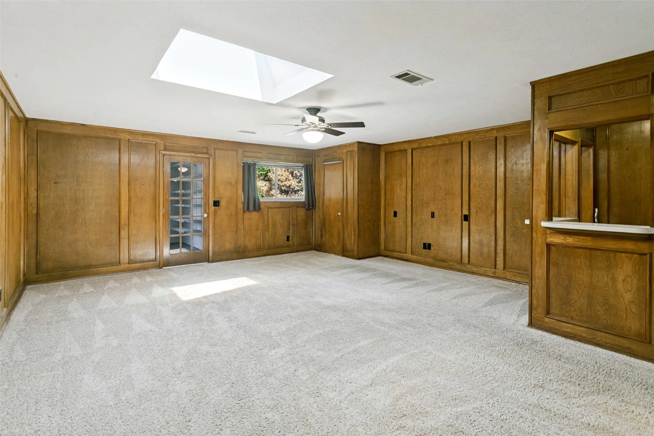 Spacious room featuring wood paneling, wall-to-wall carpeting, and a built-in wet bar with a white countertop