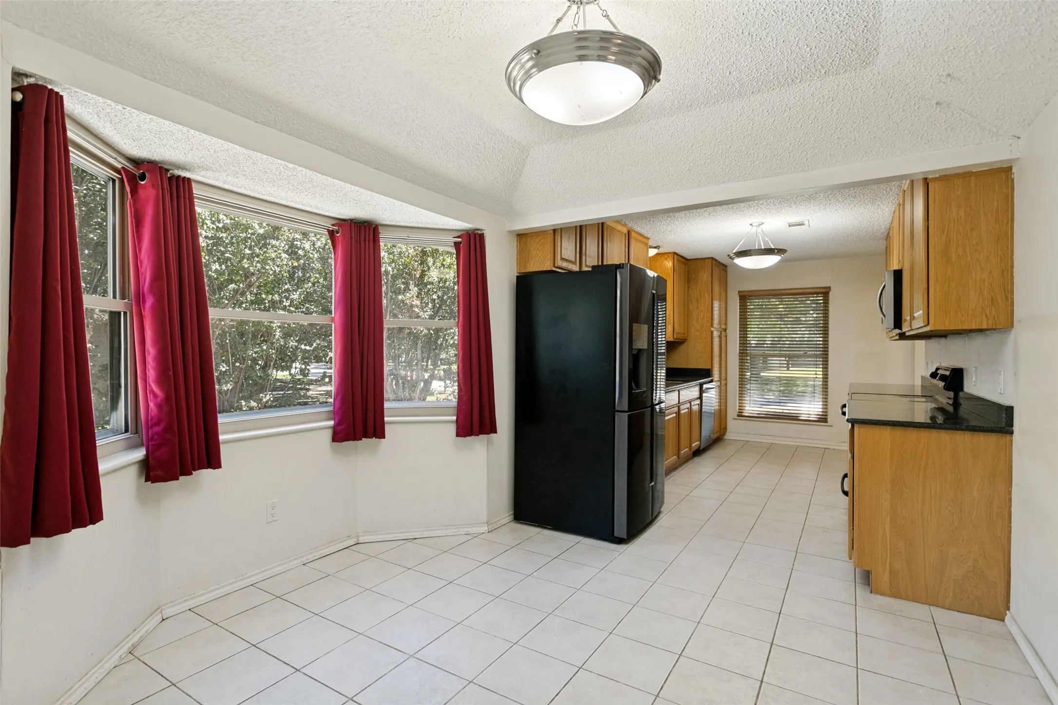 Kitchen featuring wood-finish cabinetry, black appliances, black countertops, and a tile floor