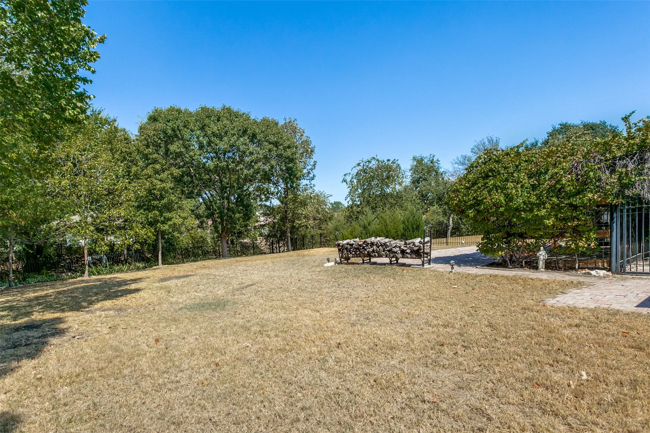 Expansive outdoor space featuring mature trees, a clear blue sky, and a paved entrance