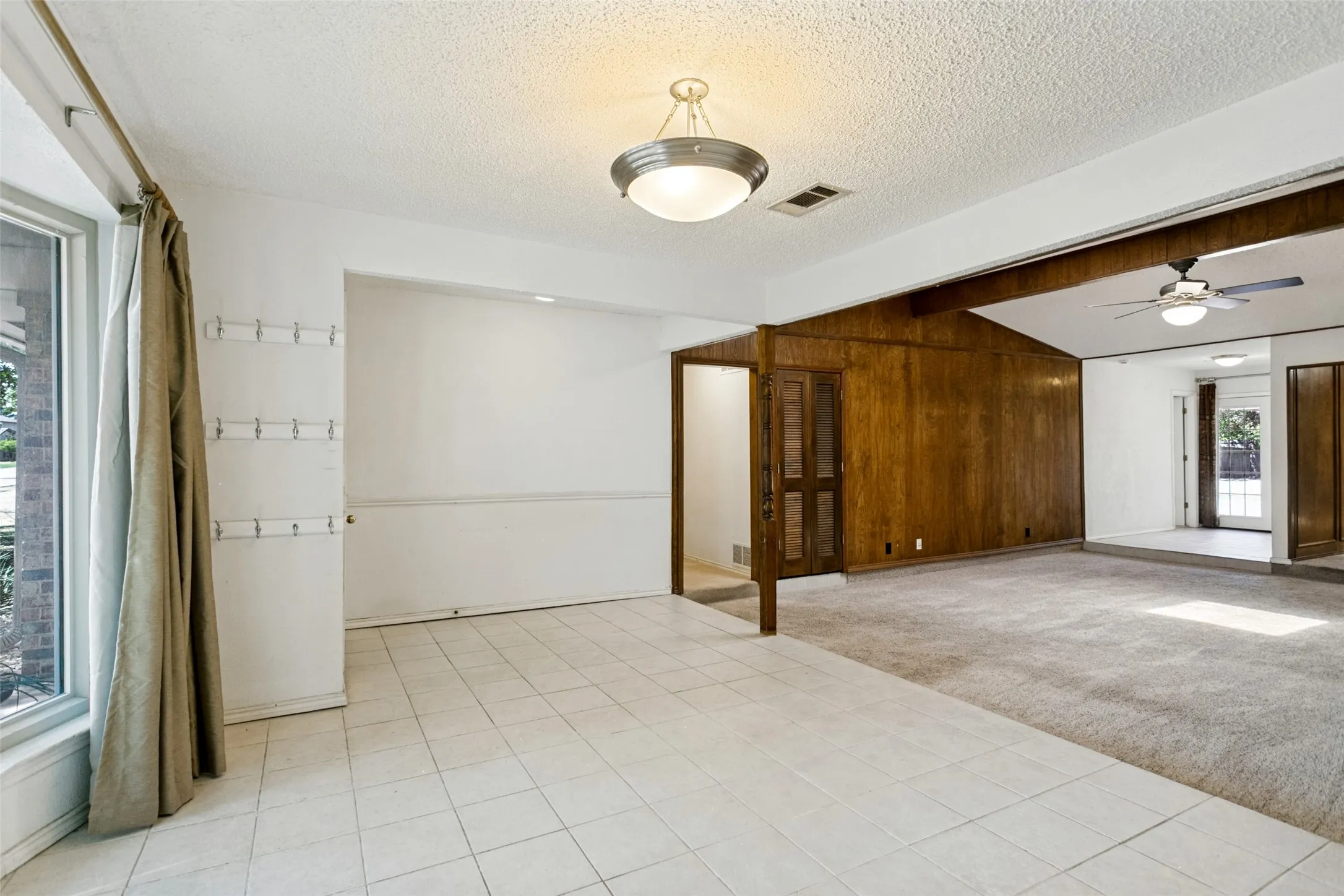 Bay window, tiled flooring, wood paneling, vaulted ceiling, and ceiling fan