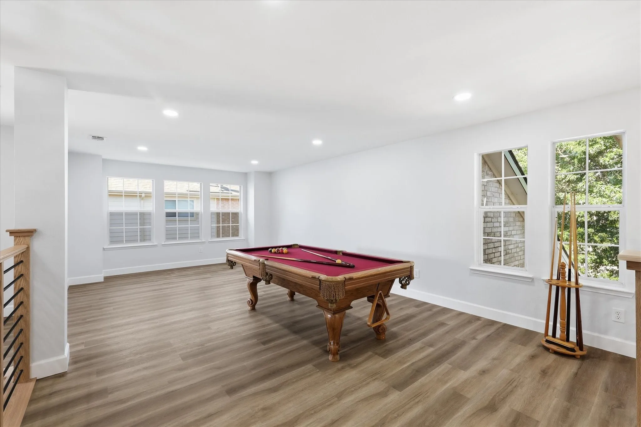 Spacious recreation room featuring wood-finish flooring, recessed ceiling lighting, and multiple large windows with transom details providing natural light