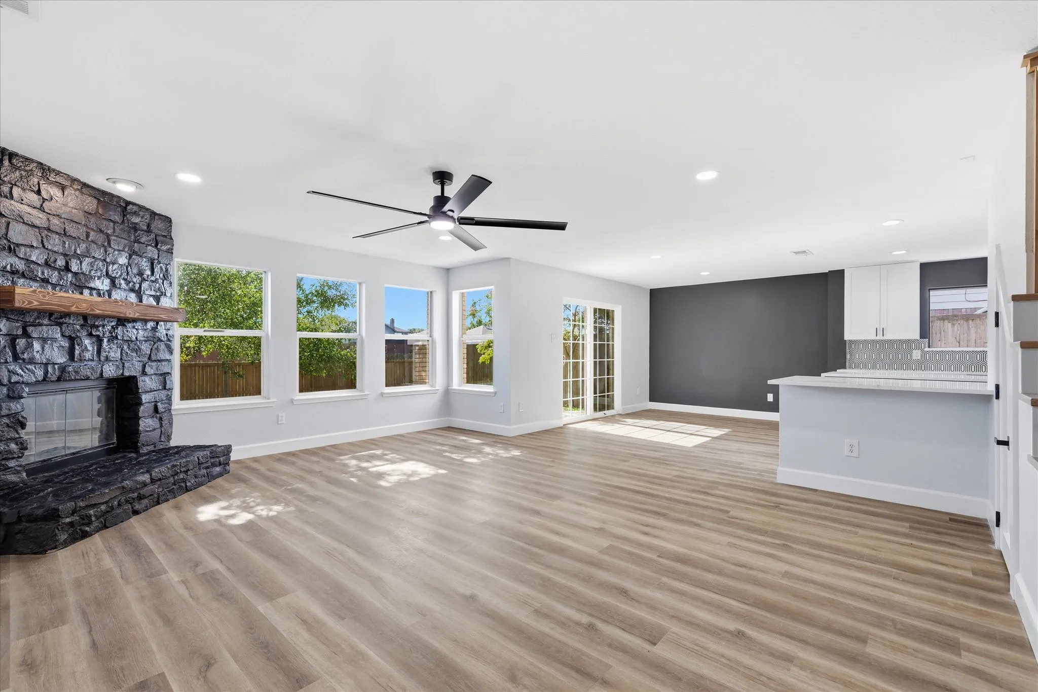 Stone-clad fireplace with wood-beam mantel, wood-finish flooring, recessed lighting, and a modern ceiling fan