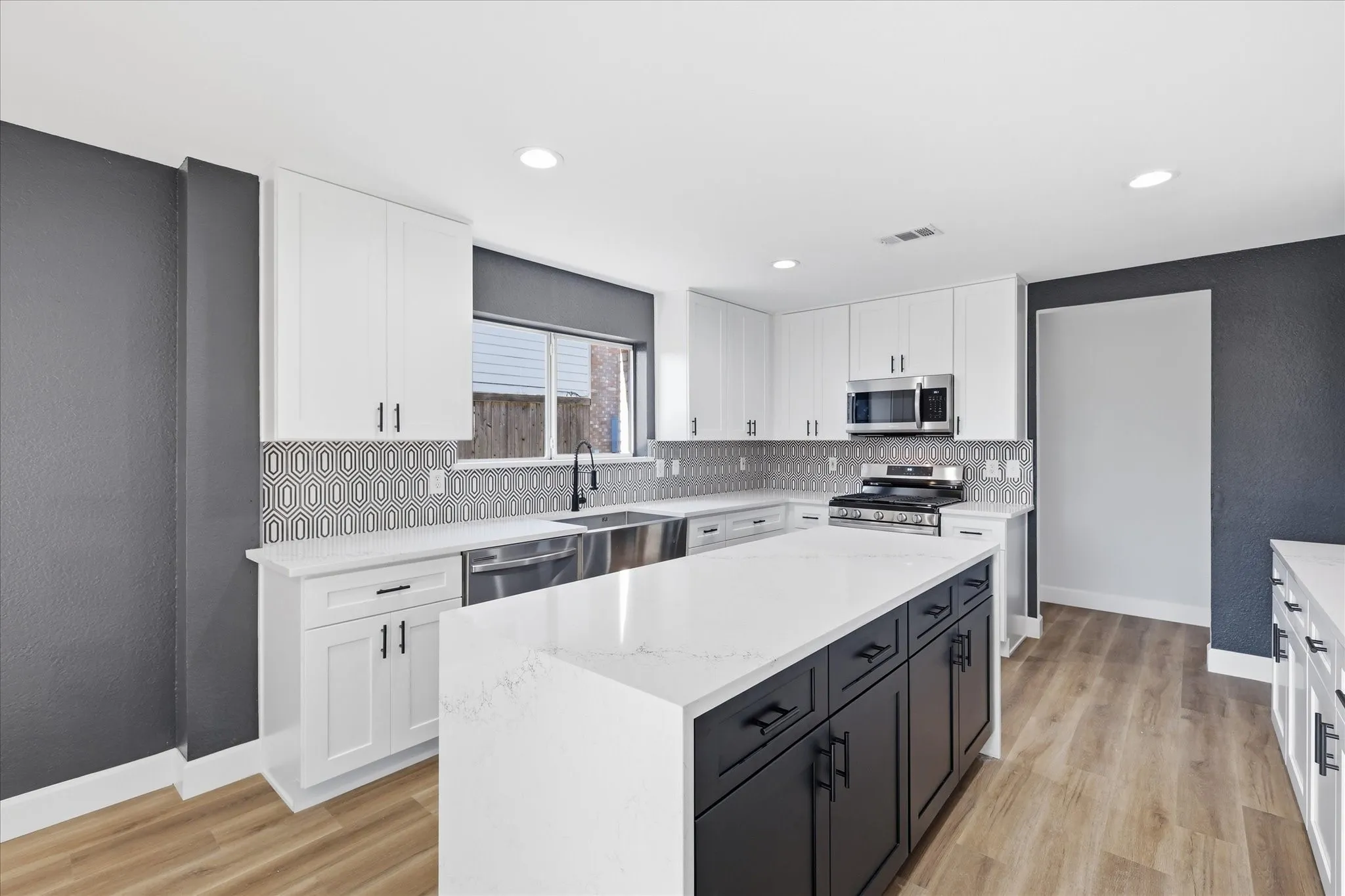 Contemporary kitchen featuring white cabinetry, a dark-toned island with storage, light-toned countertops, a geometric pattern tile backsplash, and wood-finish flooring