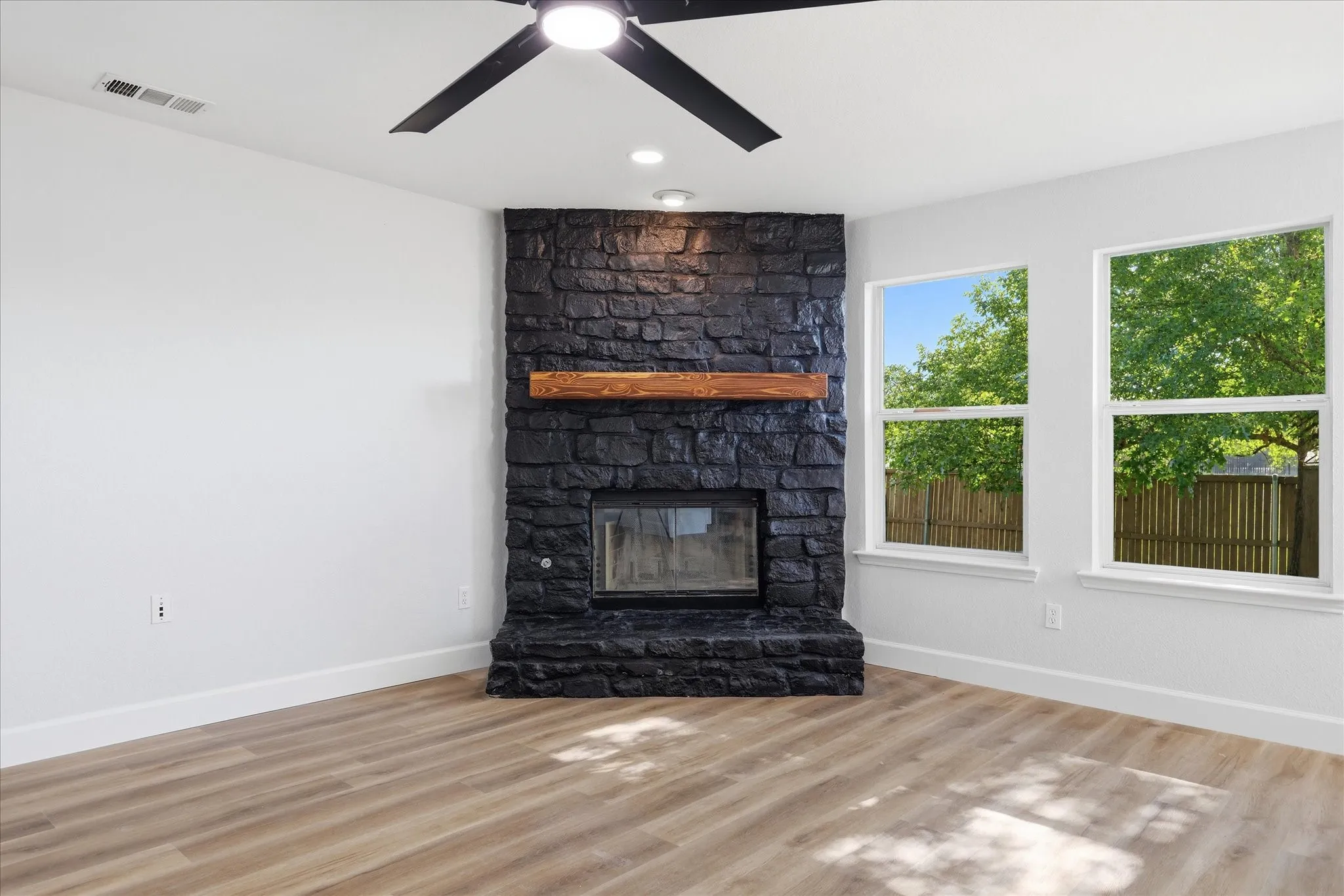 Black stone fireplace with a wood mantel, wood-finish flooring, recessed lighting, and a ceiling fan
