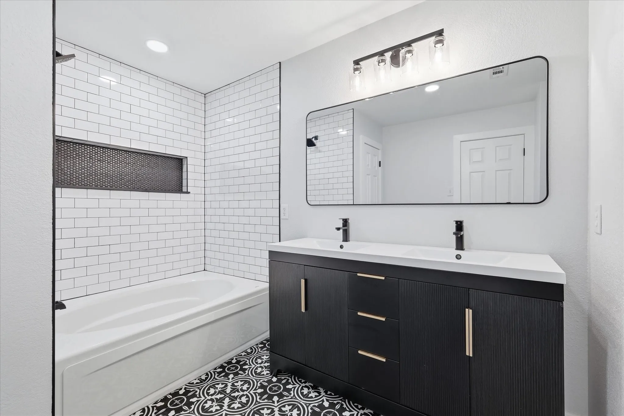 Bathroom featuring a double vanity with matte black finish and gold-tone hardware, a large rectangular mirror, and a tub-shower combination with white subway tile surround